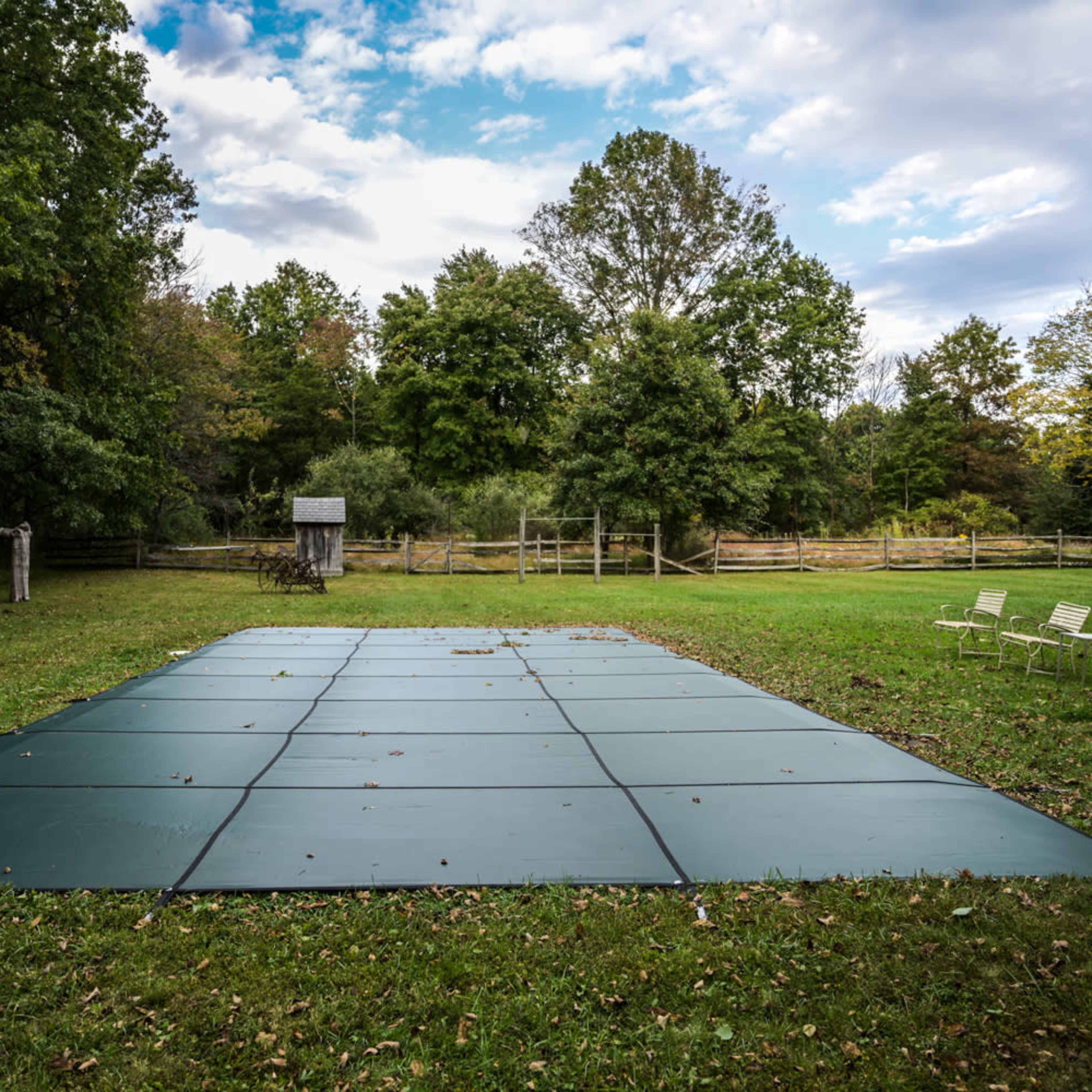 A large green area covered by rectangular mats in a grassy landscape with trees and a small structure in the background.