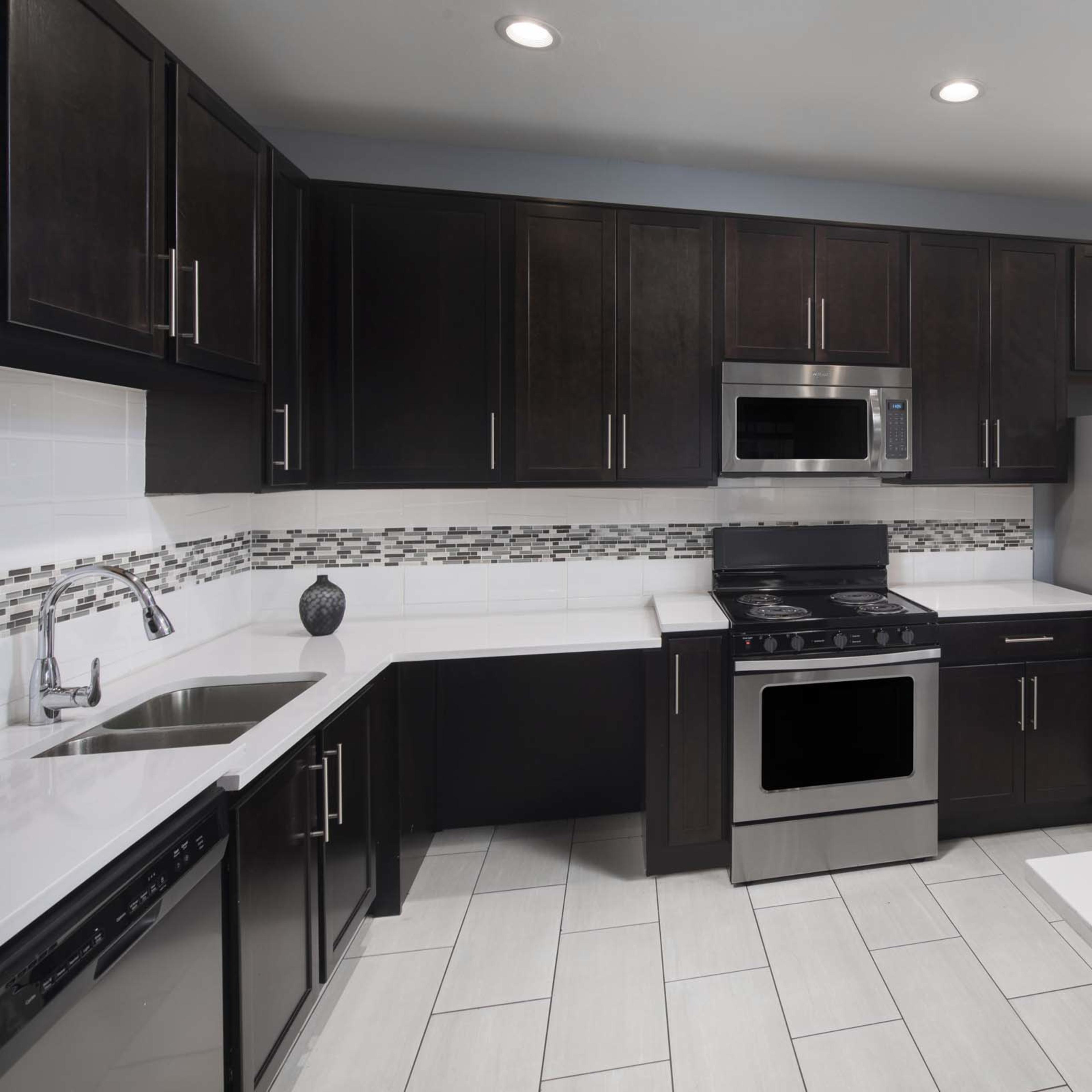 A modern kitchen with dark cabinetry, stainless steel appliances, and tiled flooring.