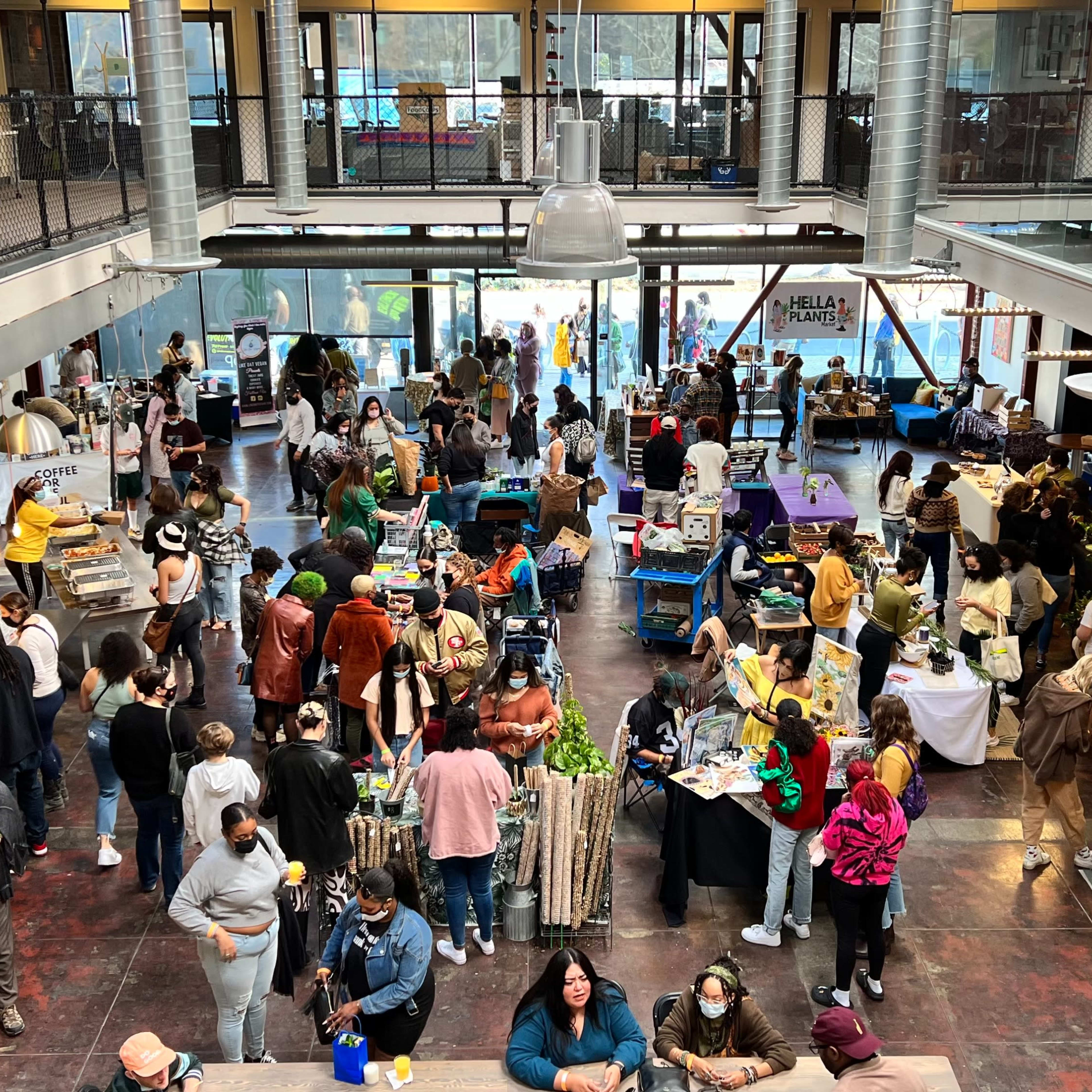 A bustling indoor market with numerous vendors and visitors engaging in various activities around a large, open space.