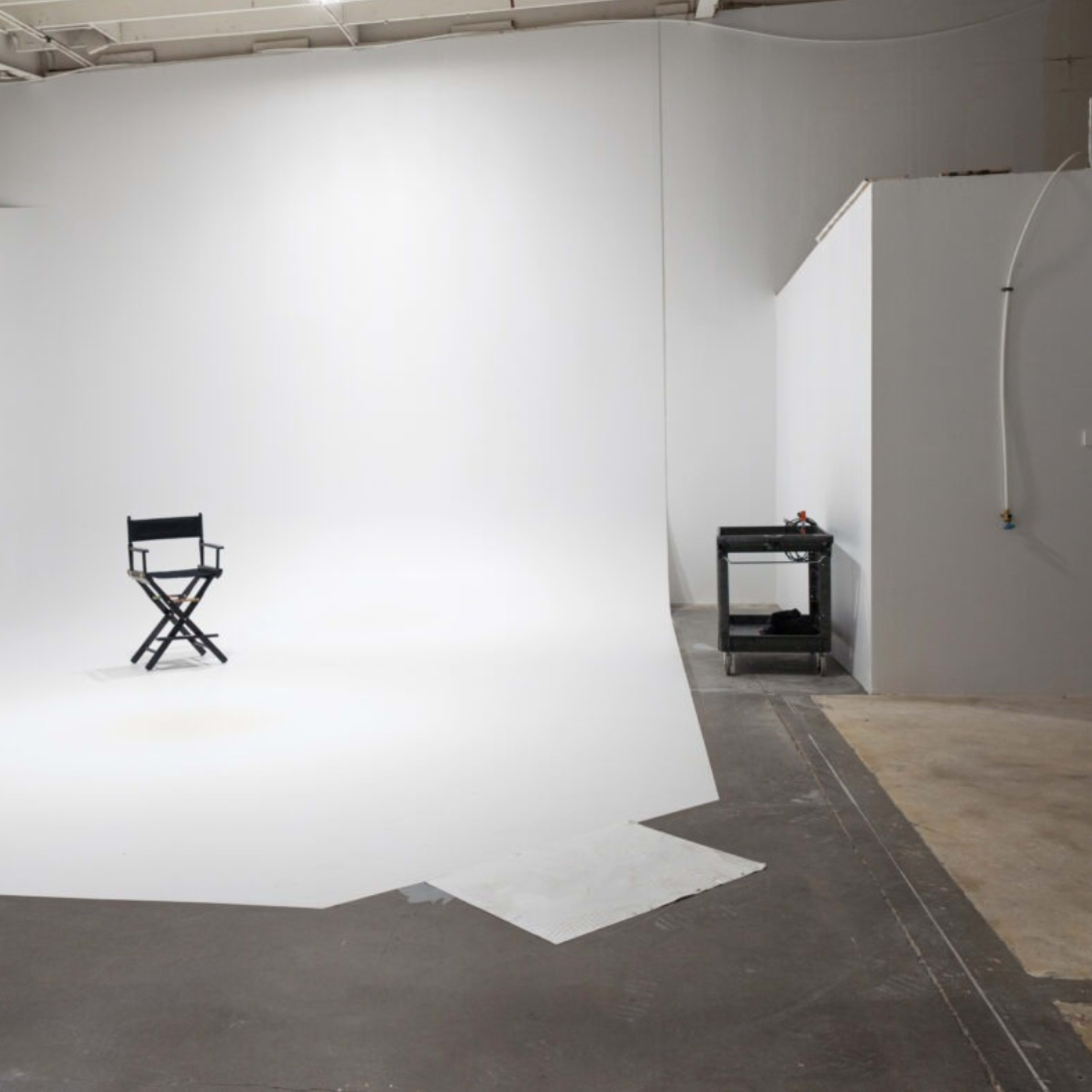 A single director's chair is positioned on a vast, empty white backdrop within a studio space.