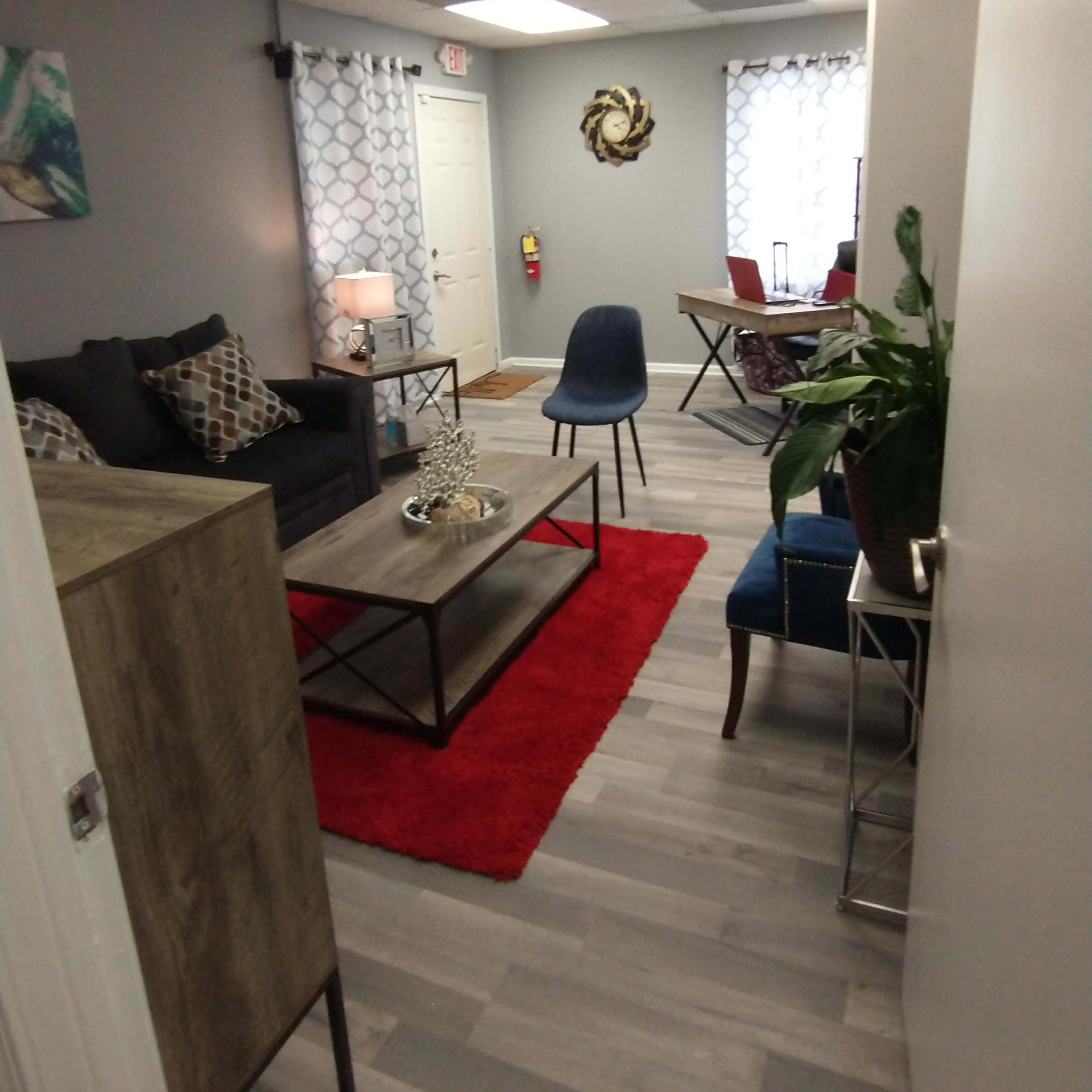 A modern, welcoming office space with a seating area featuring a sofa, coffee table, and decorative rug, alongside a small dining table and chairs.