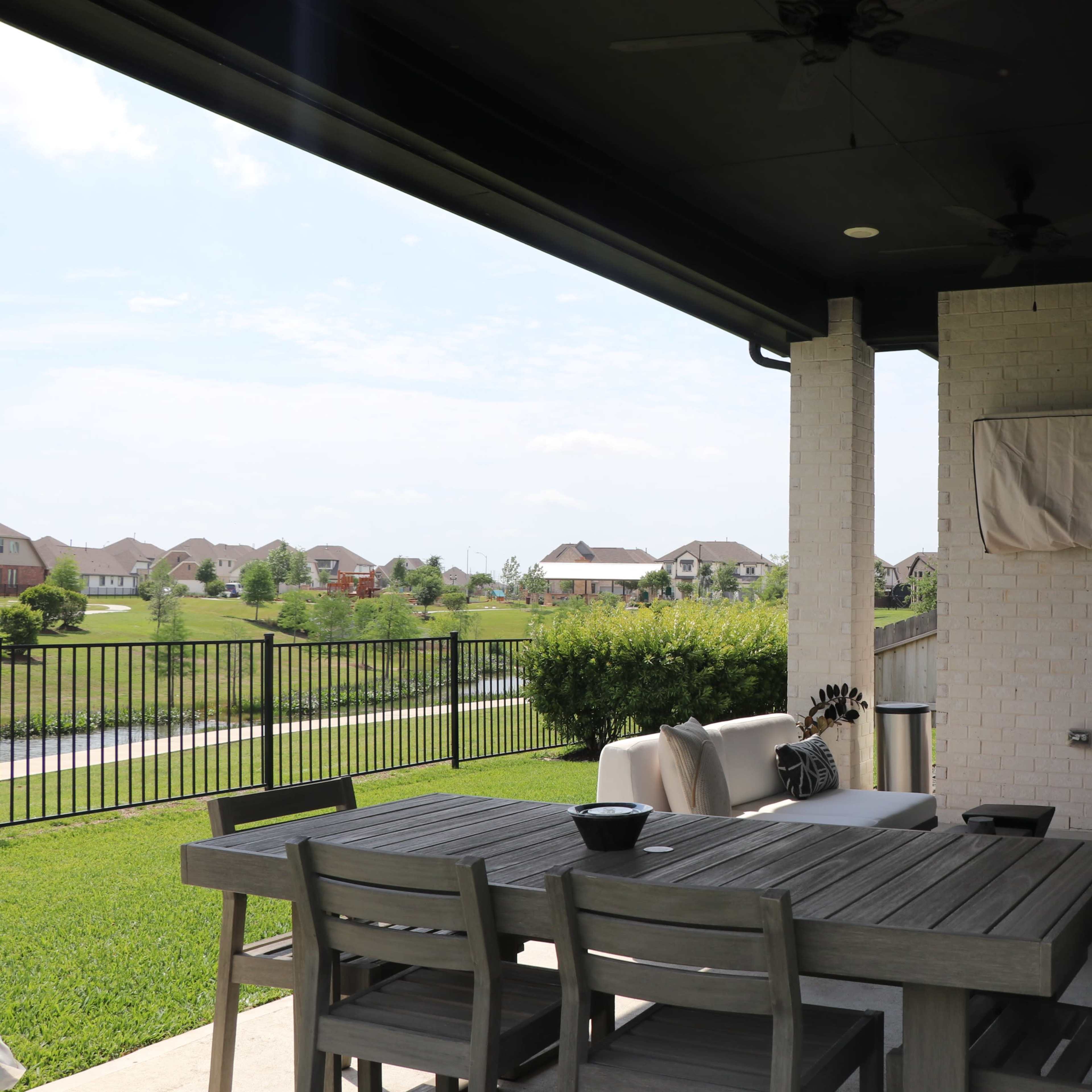 A patio with a dining table and chairs overlooks a grassy area and houses in the distance.