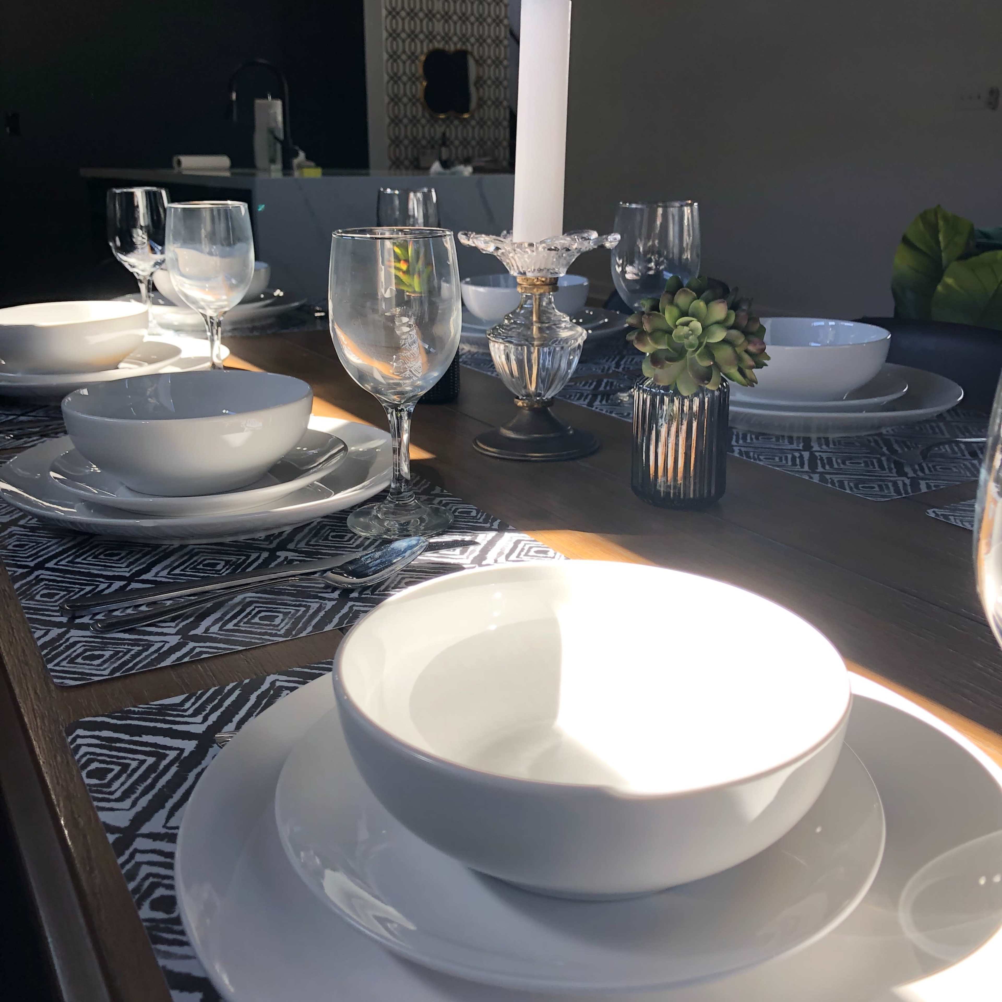 A dining table is set with white dishware, glassware, and a decorative candle in the center.