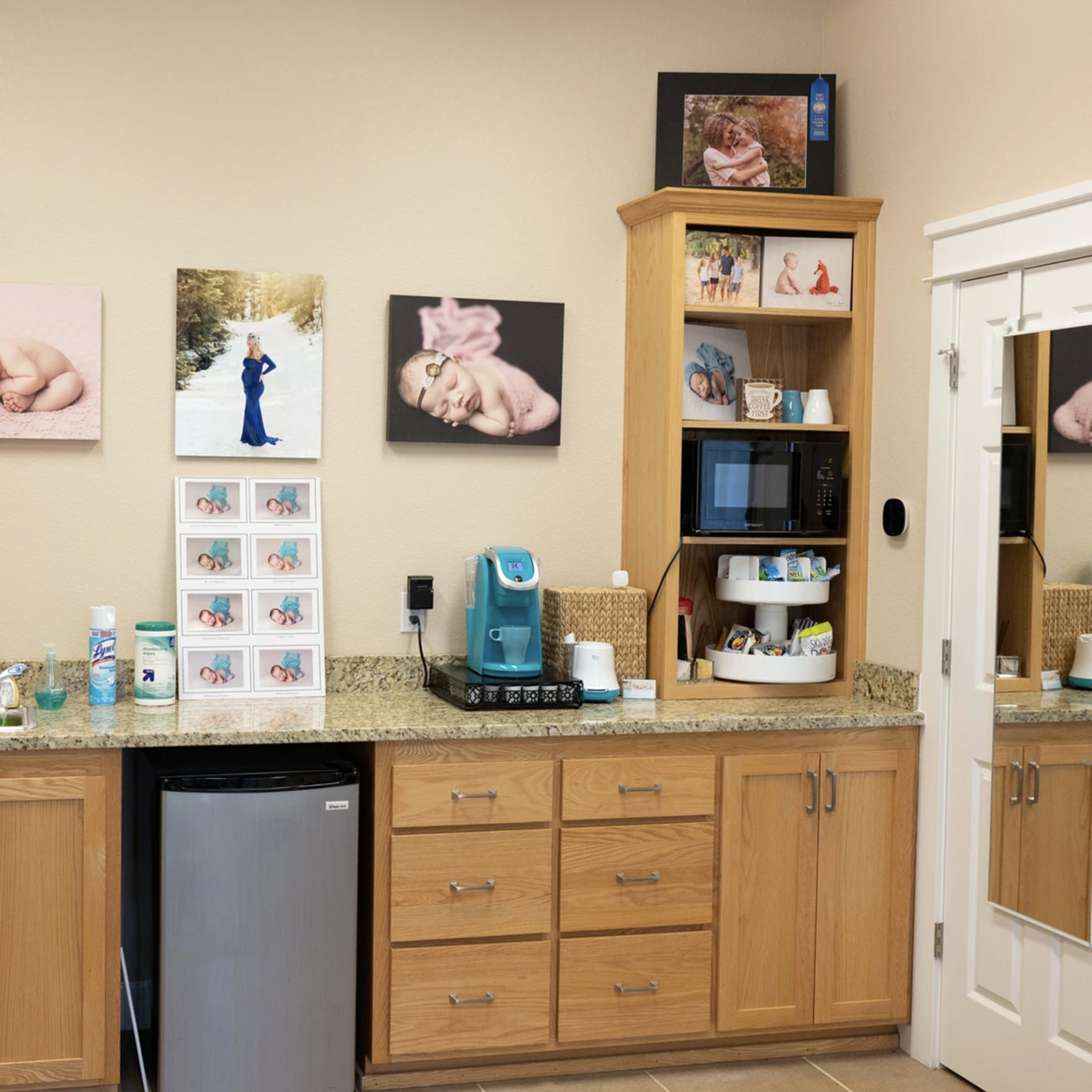 A well-organized room with wooden cabinetry, a small refrigerator, and framed photographs on the walls.