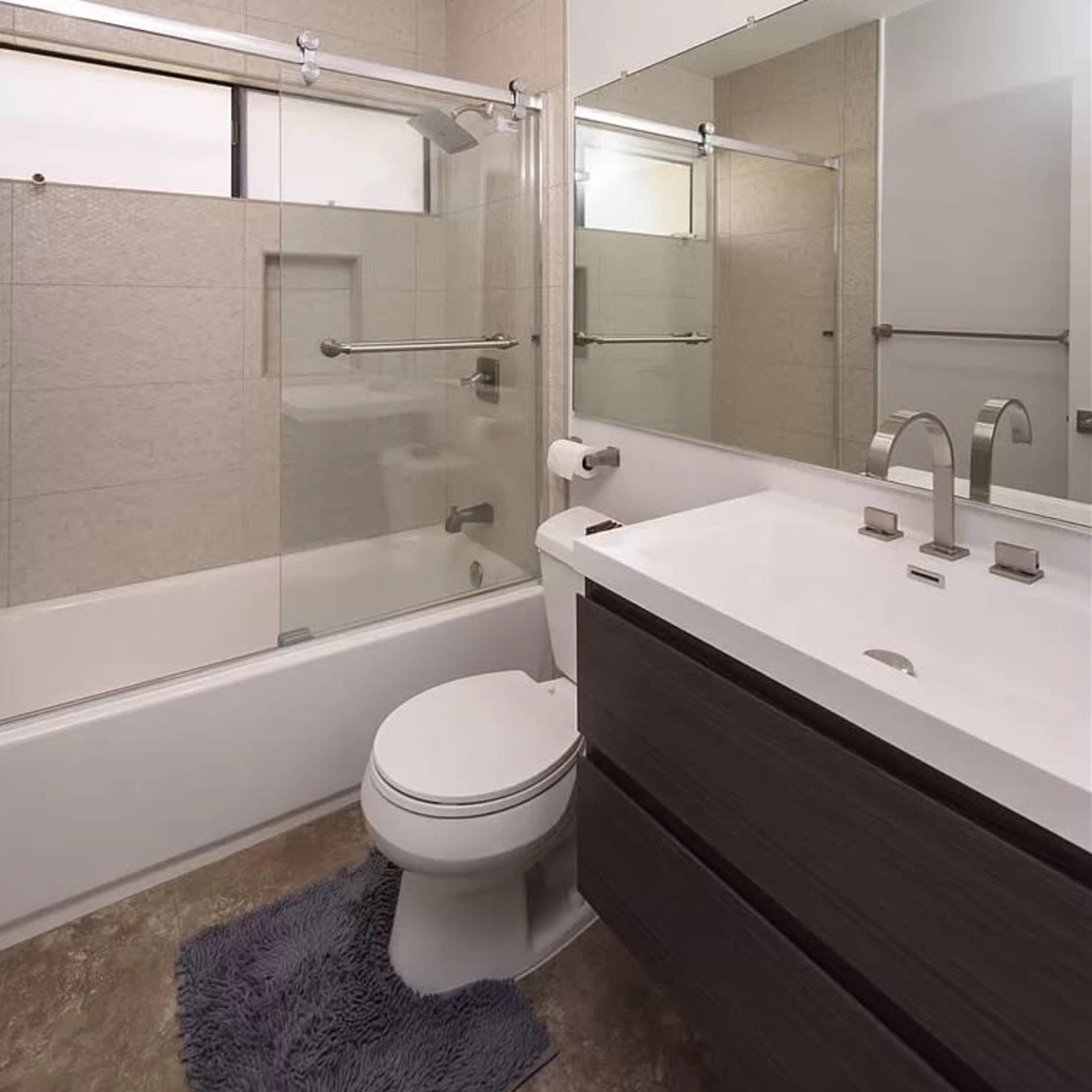 A modern bathroom featuring a glass shower enclosure, a bathtub, a toilet, and a sleek vanity with a large mirror.