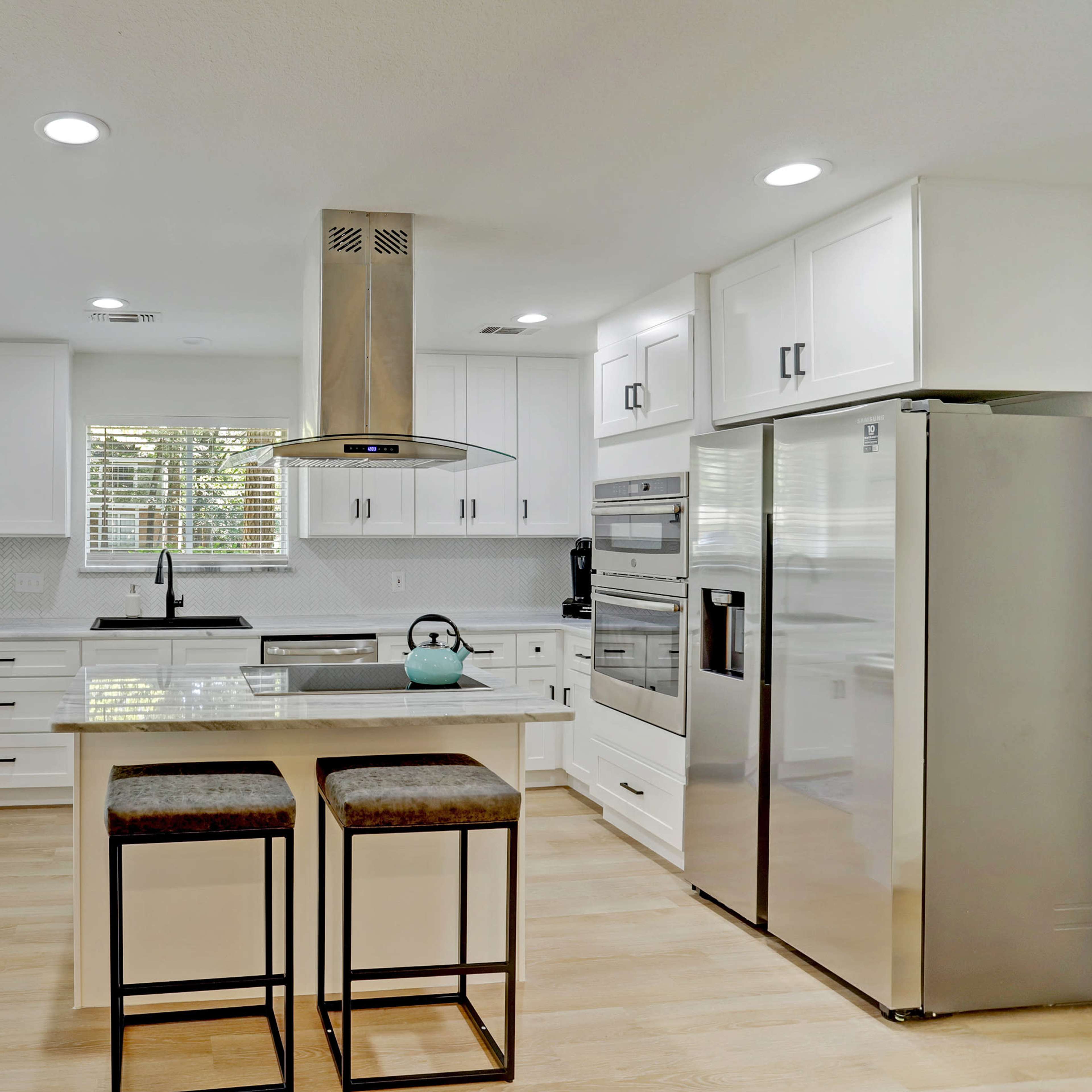A modern kitchen features white cabinets, stainless steel appliances, and two bar stools at a central island.