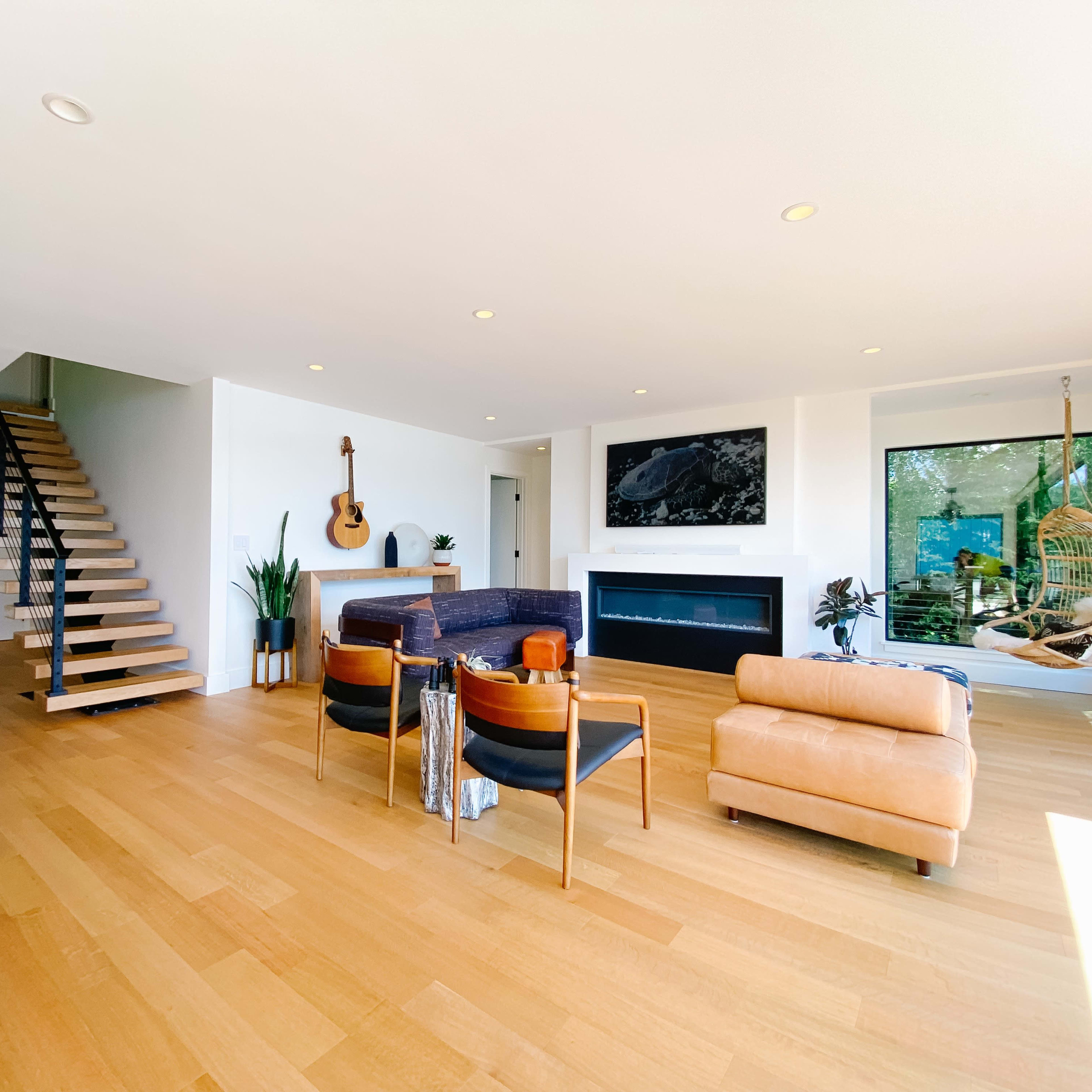 A modern living room with hardwood floors, a fireplace, a guitar on the wall, and a staircase leading to an upper level.