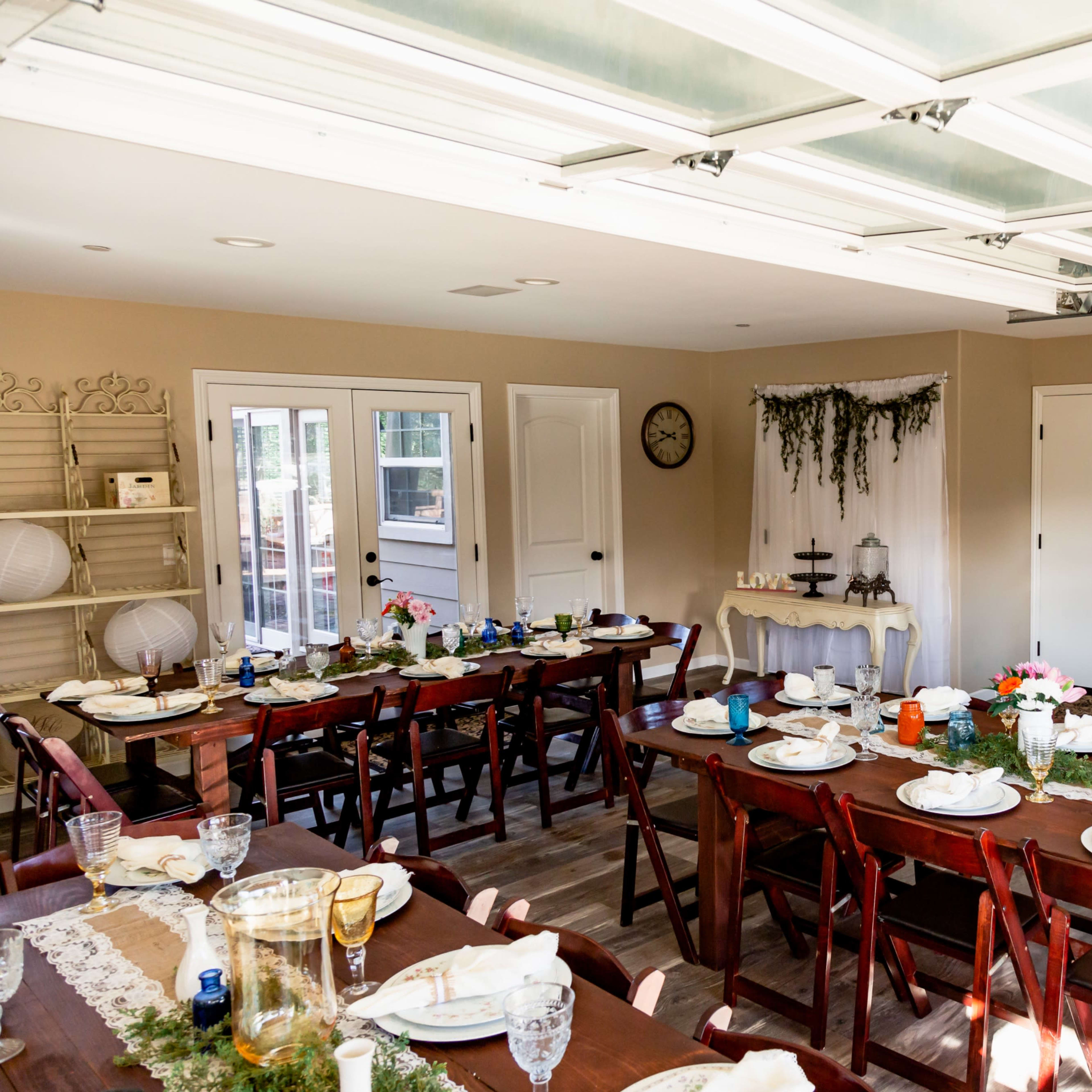 A dining room is set up with multiple tables arranged for a meal, decorated with place settings and floral arrangements.