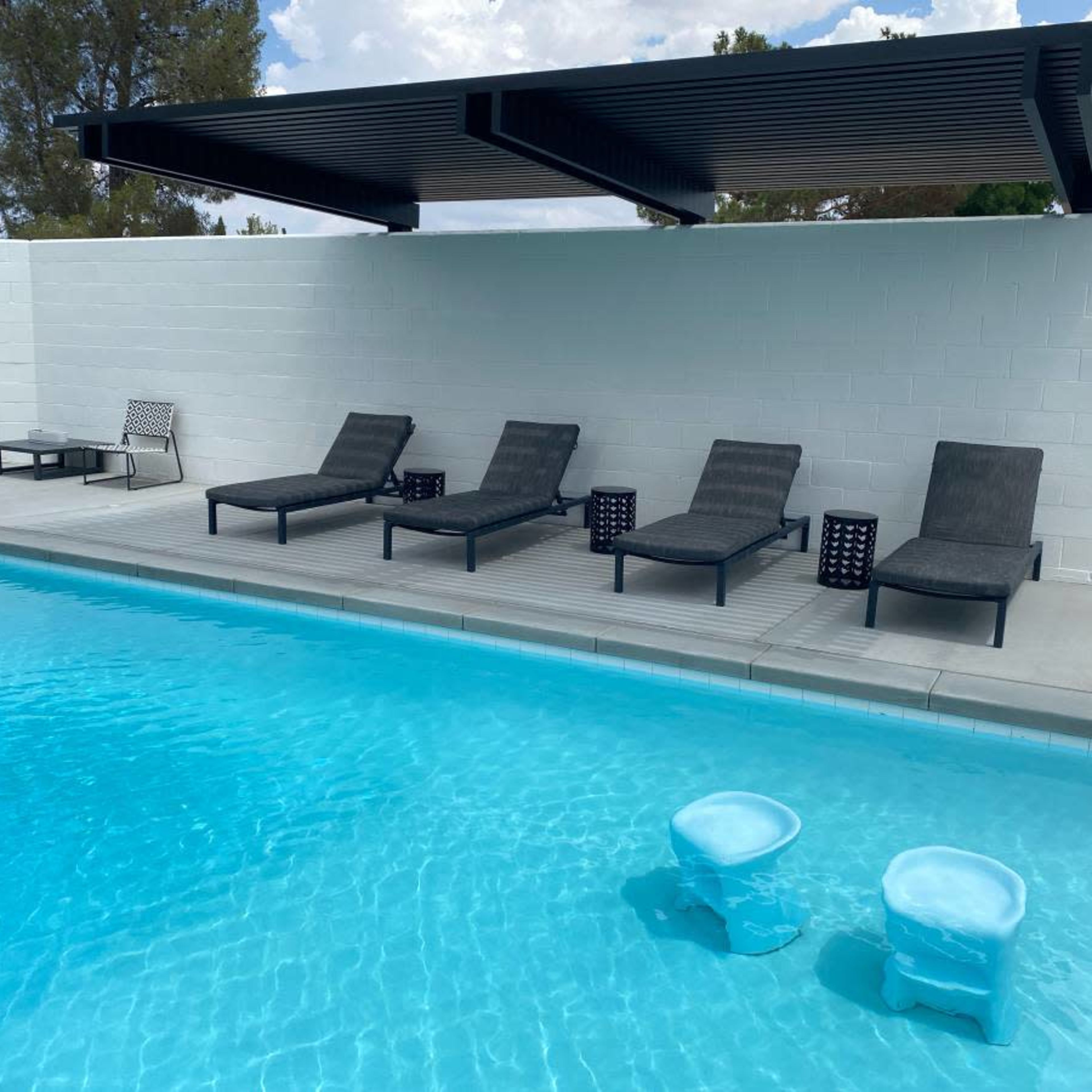 A modern swimming pool with five lounge chairs and two small tables on the deck beside the water.