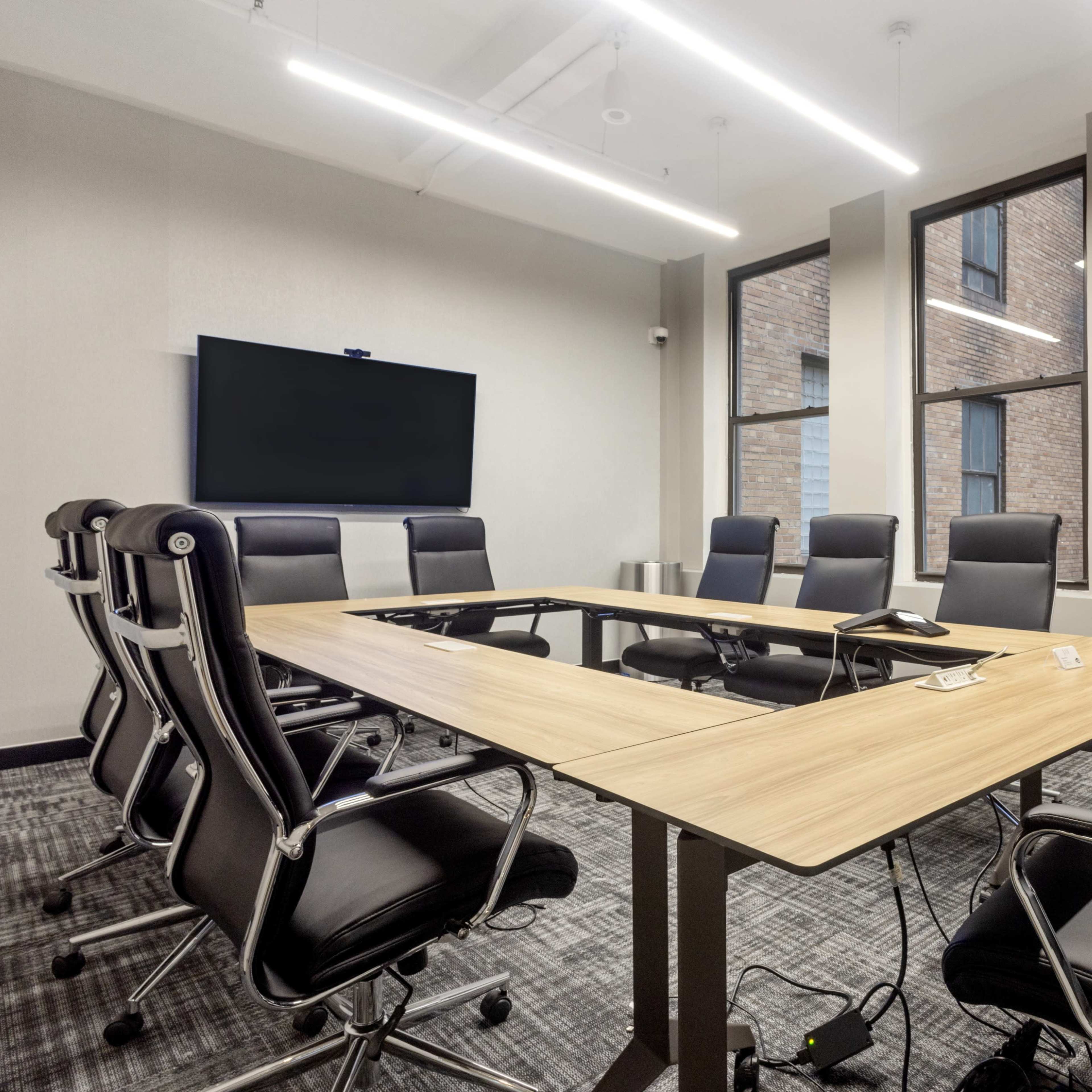 A conference room features a large wooden table surrounded by black leather chairs and a wall-mounted screen.