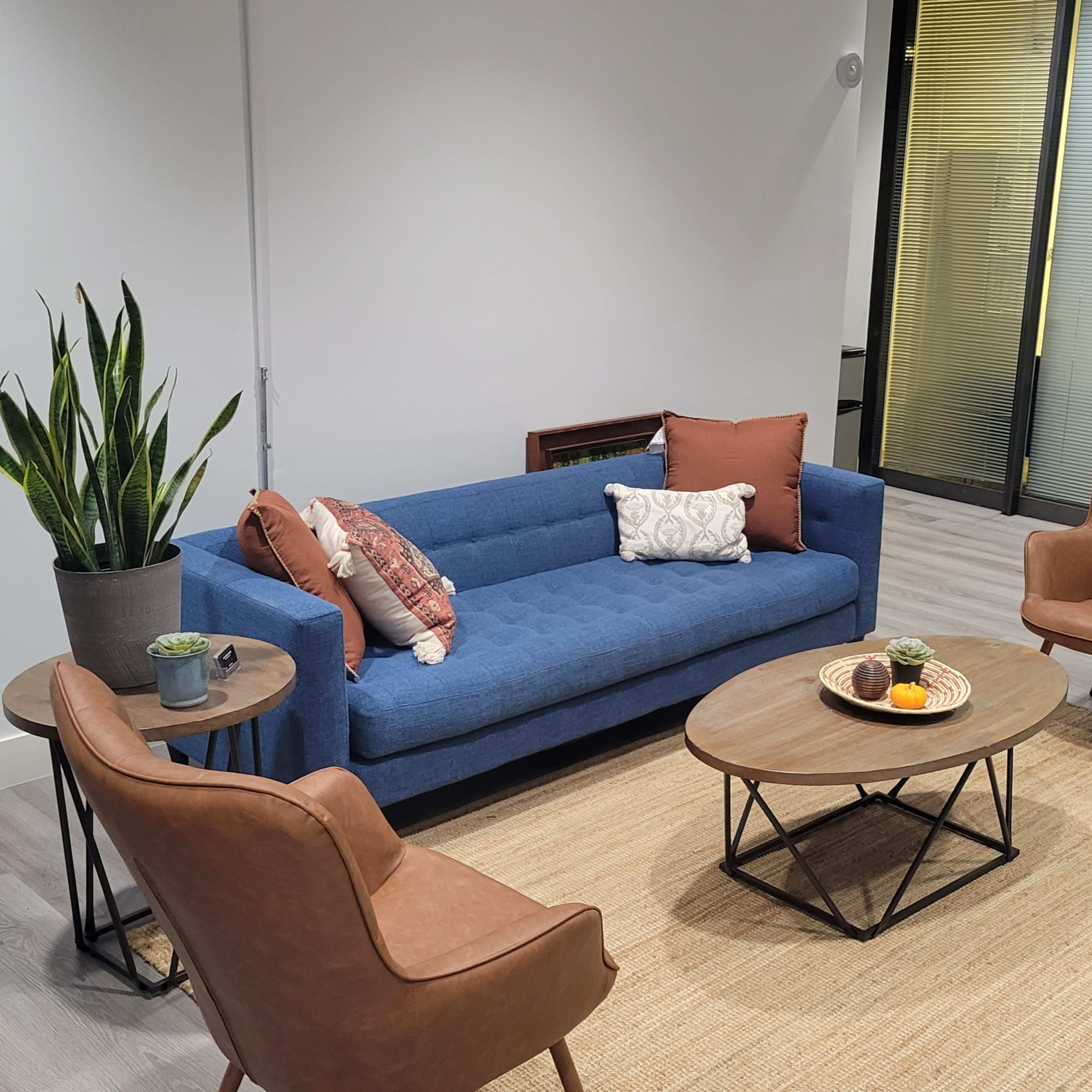 A modern room with a blue sofa, two brown armchairs, and a round coffee table, all arranged on a light-colored rug.