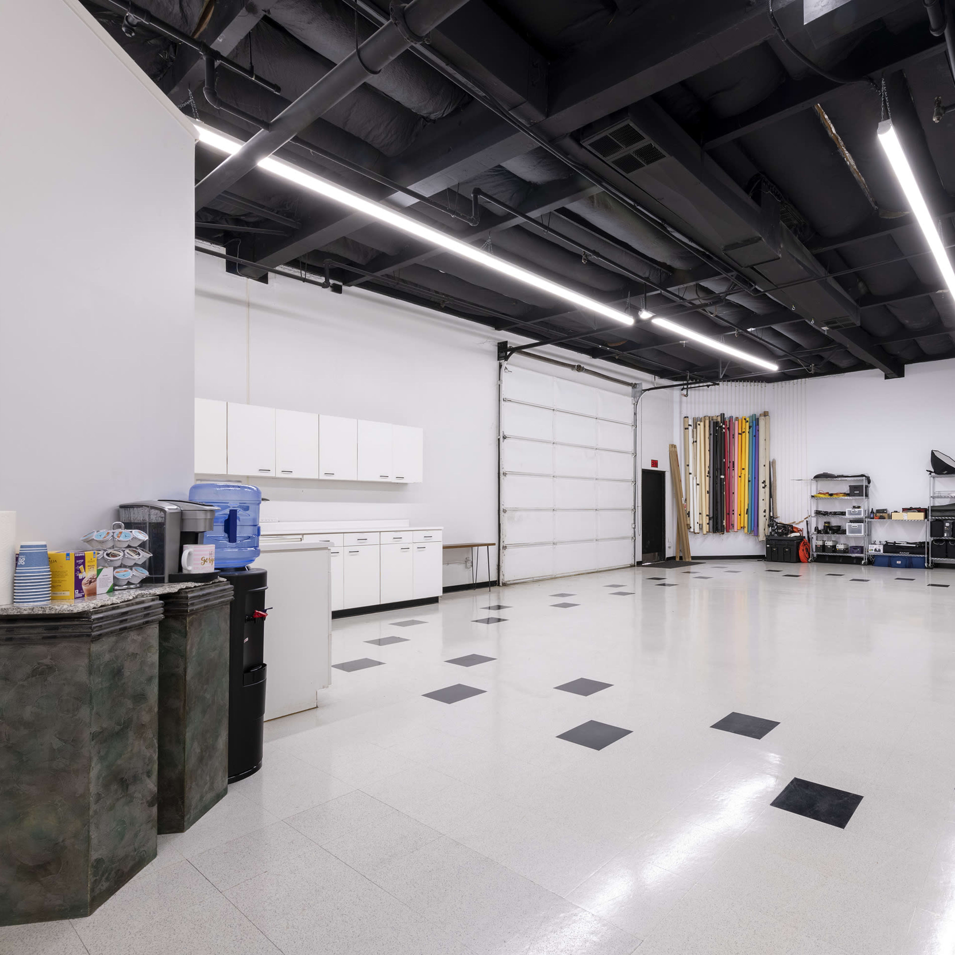 A spacious, well-lit room with a polished floor, featuring cabinets, a water cooler, and various workstations along the walls.
