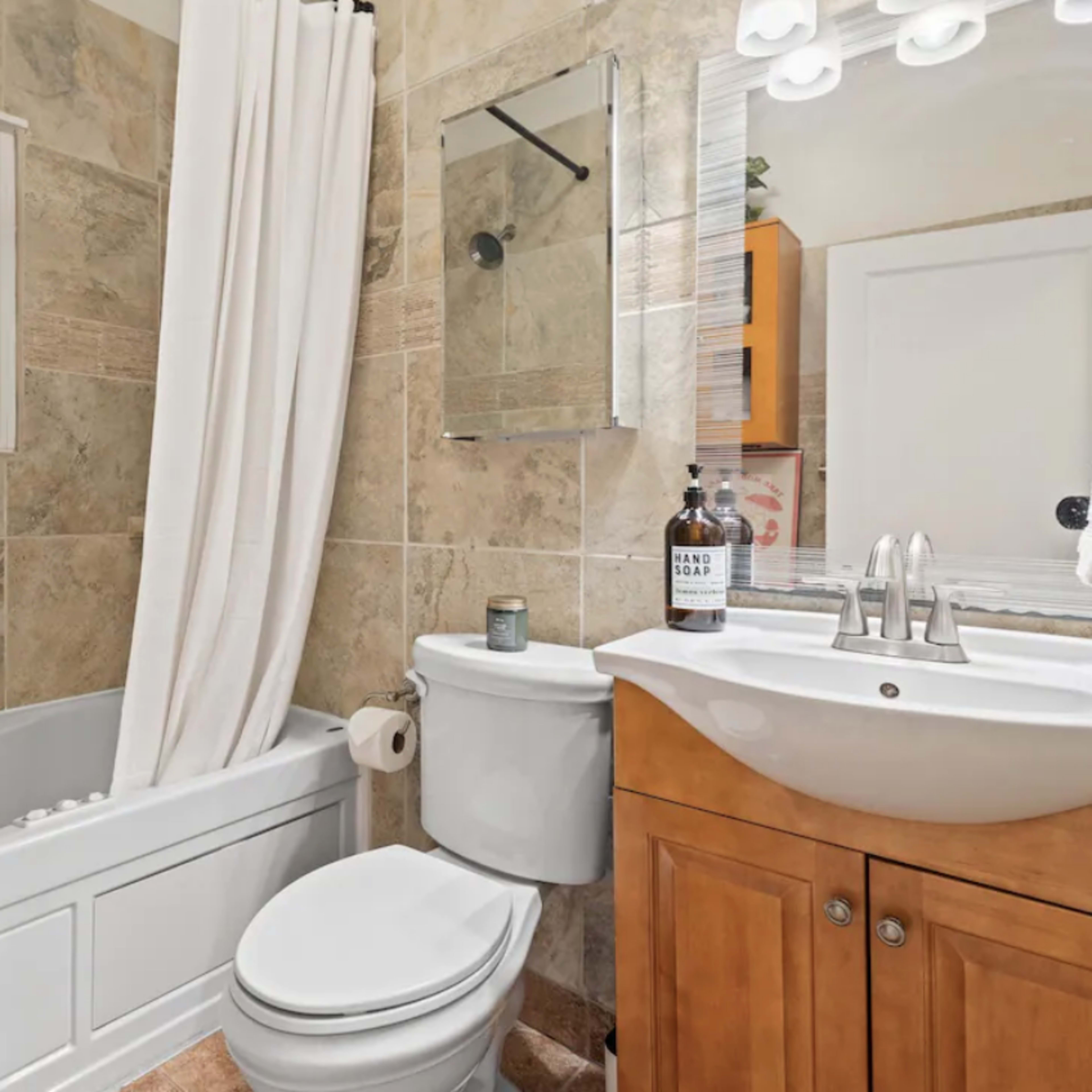 A compact bathroom with a bathtub, toilet, and a sink with wooden cabinetry, all featuring tiled walls.