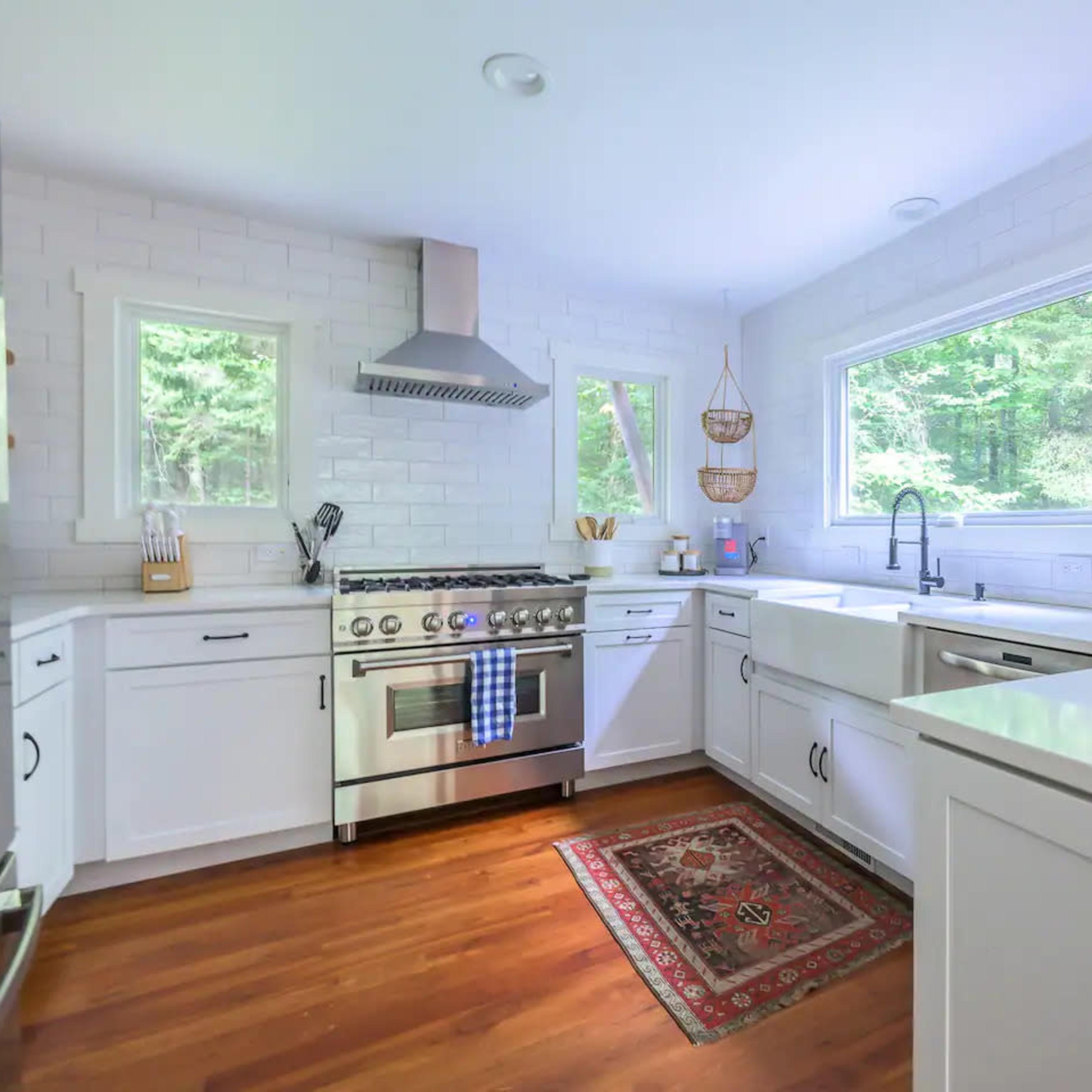 A modern kitchen features stainless steel appliances, white cabinetry, and a wooden floor with a patterned rug.