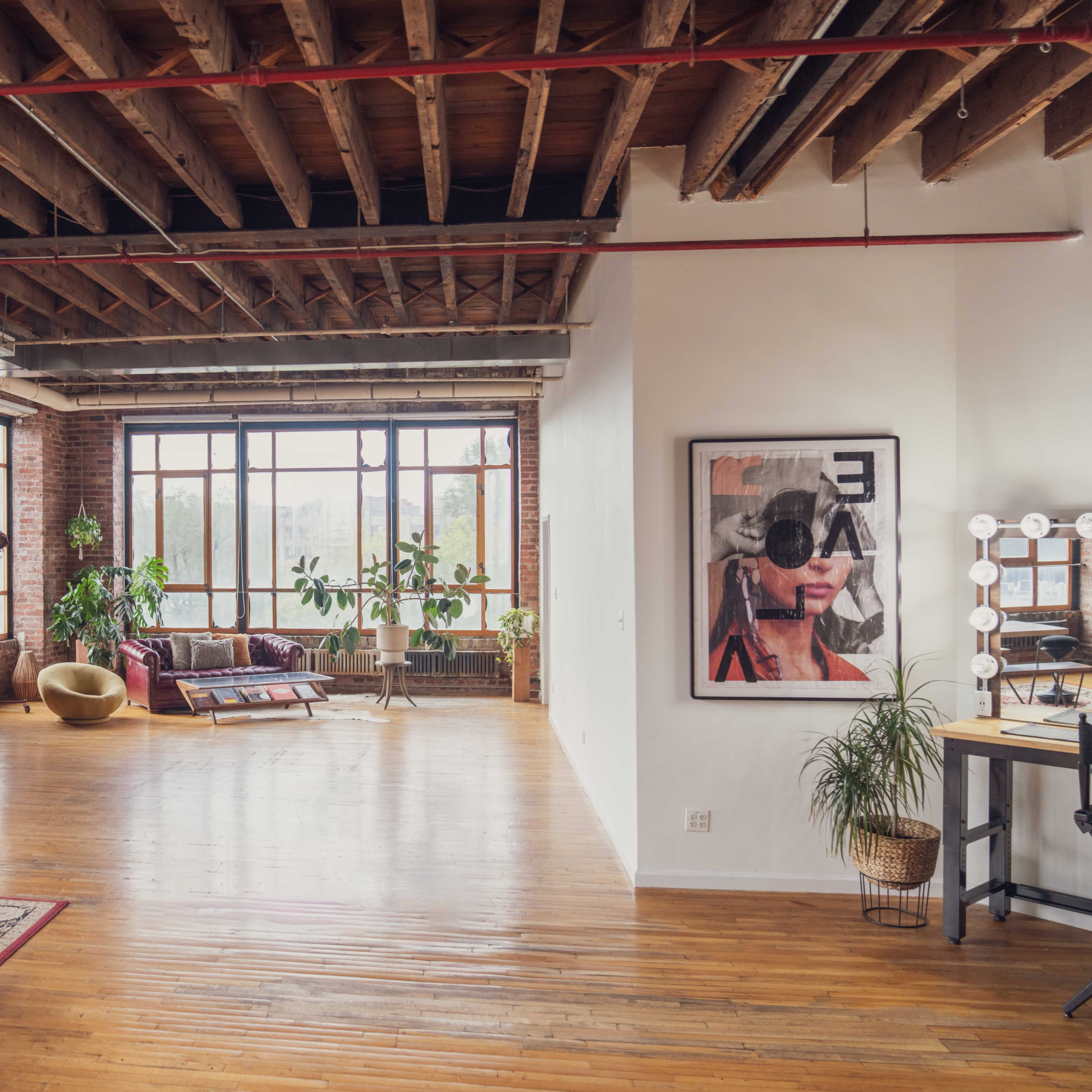 A spacious loft with exposed brick walls, large windows, wooden beams, and a mix of modern and rustic furniture.