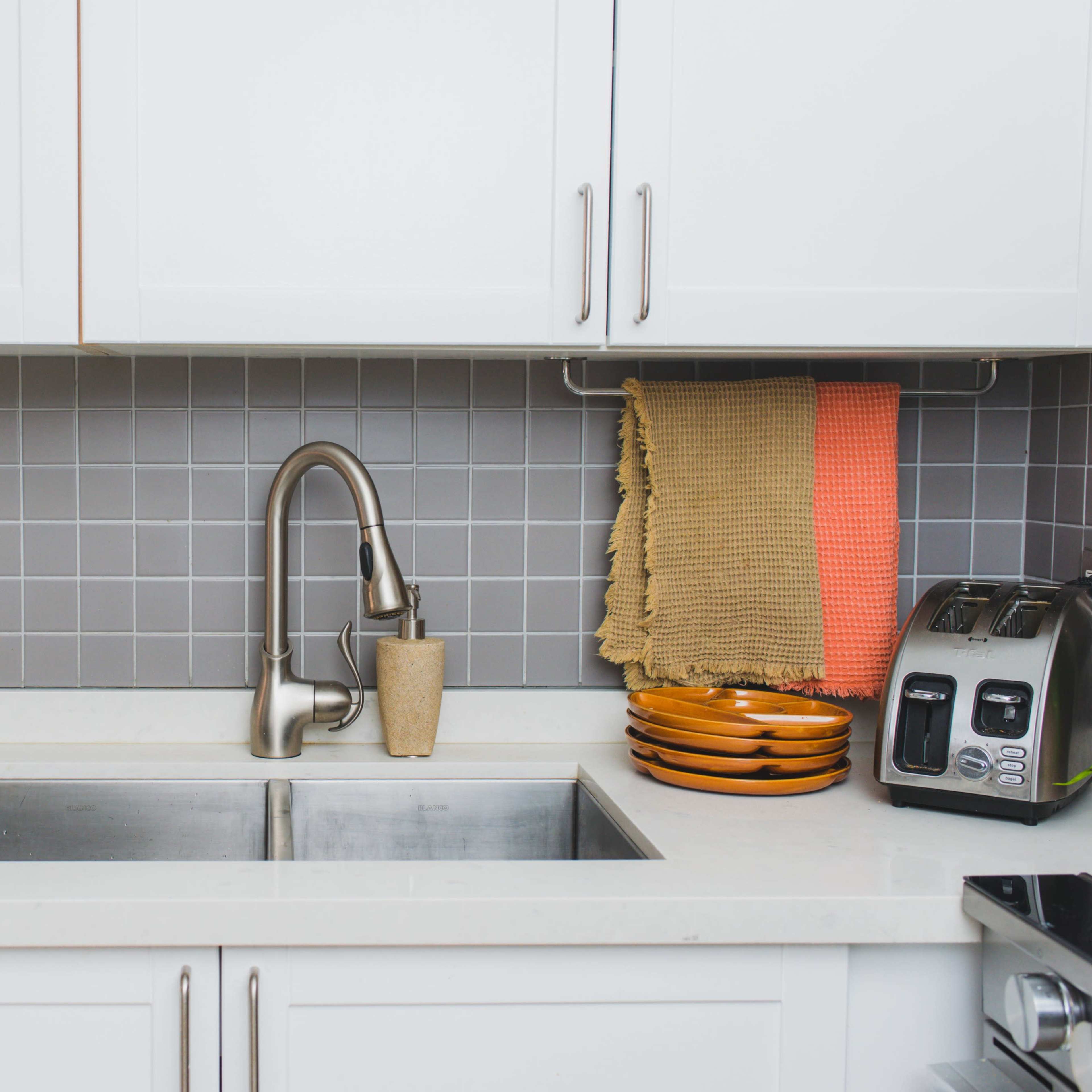 A modern kitchen with a stainless steel sink, a faucet, a countertop, and various kitchen items, including plates and a toaster.