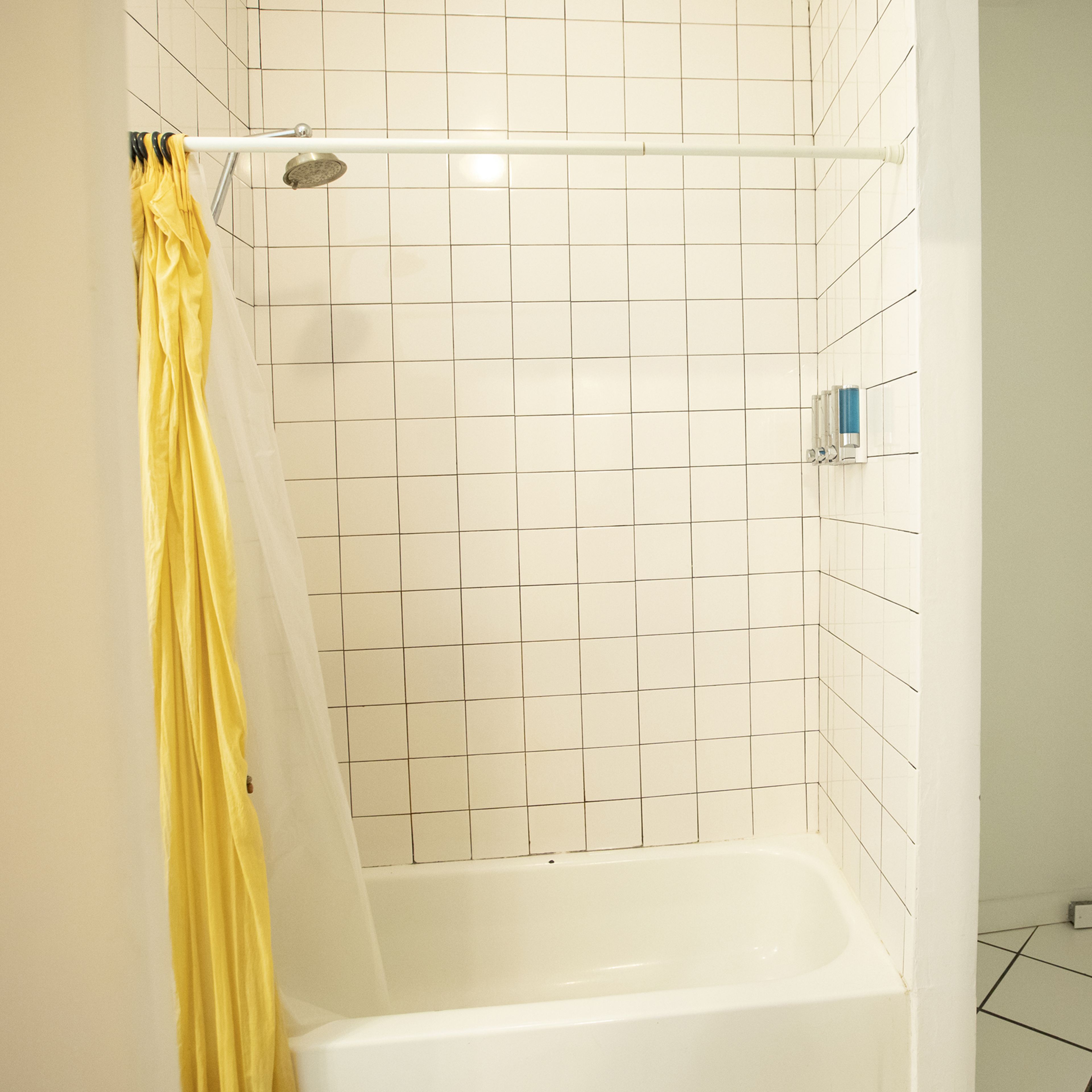 A bathroom with a bathtub and a shower curtain yellow, set against a tiled wall.