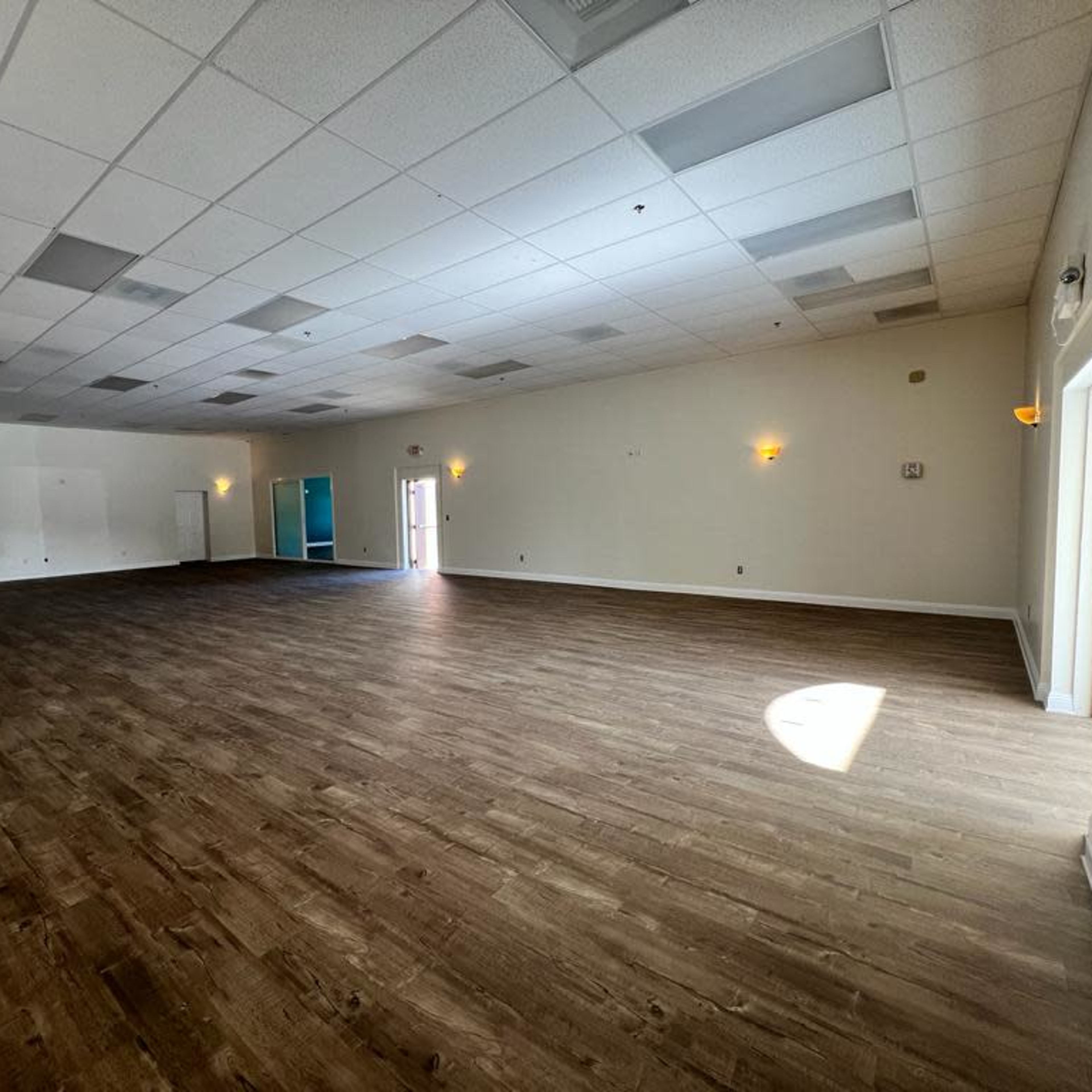 A large, empty room with wooden flooring, white walls, and several ceiling lights.