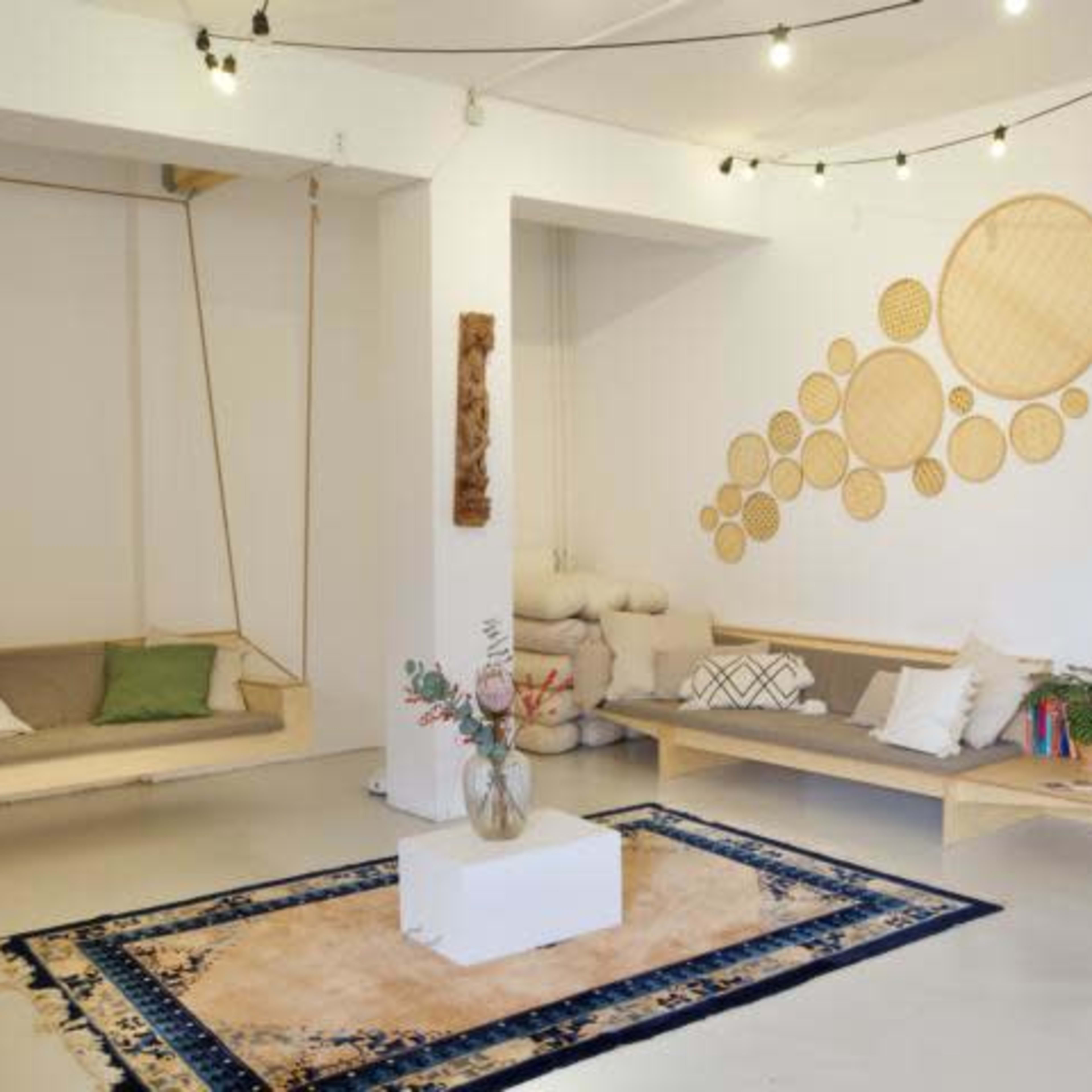 A minimalist living space featuring a wooden swing, a low wooden bench, a patterned rug, and decorative wall art made of circular wooden elements.