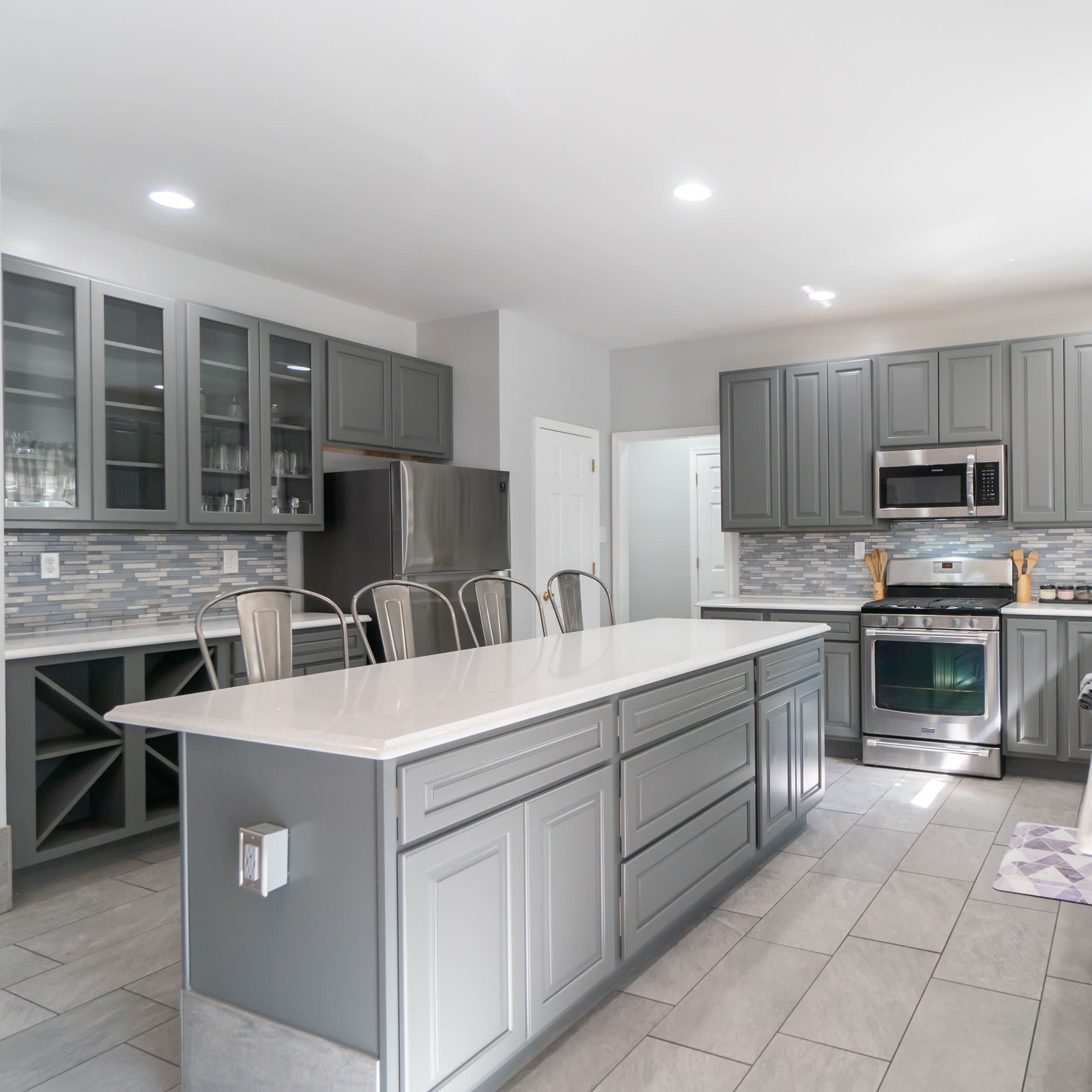 A modern kitchen with gray cabinets, a large island, stainless steel appliances, and a tile floor.