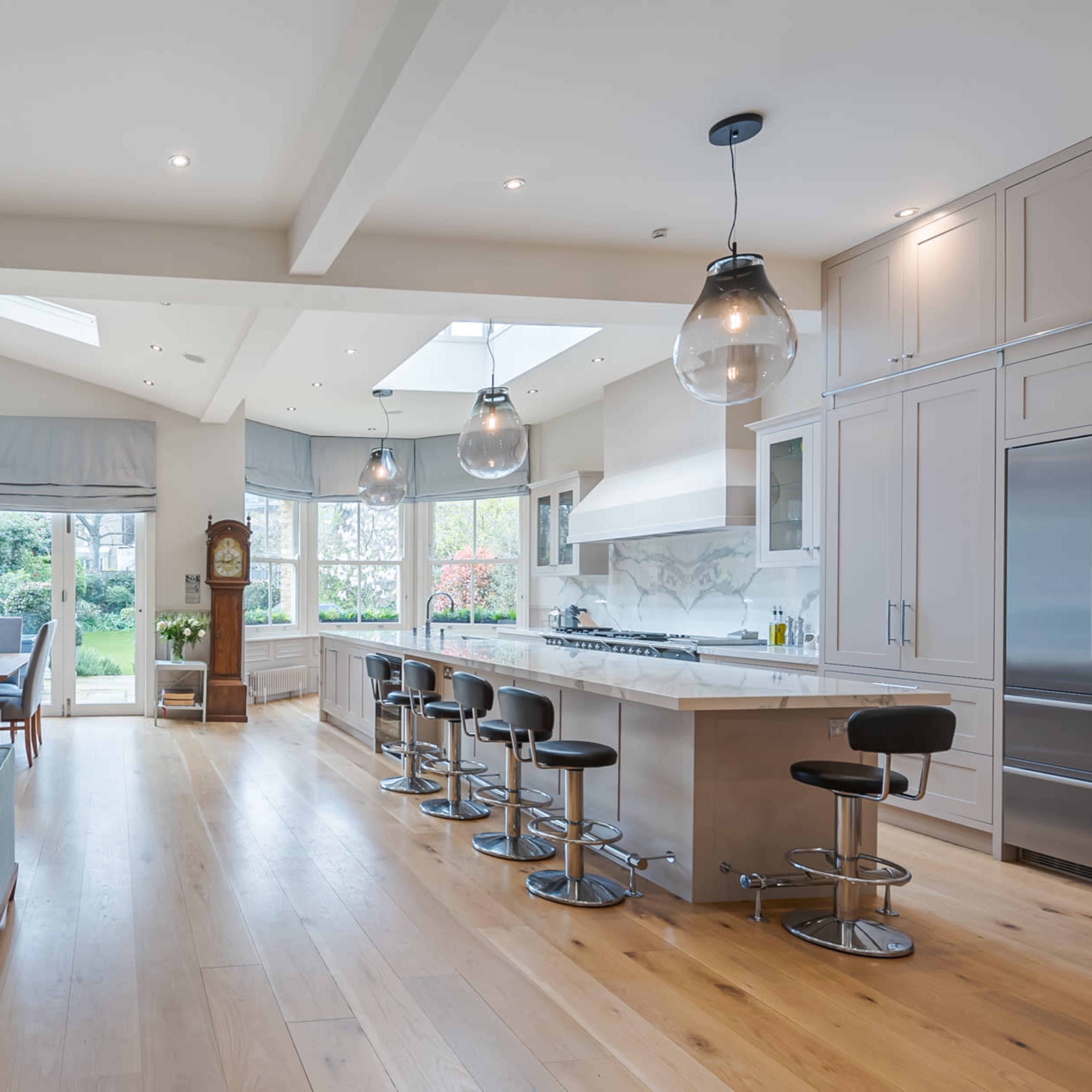 A modern, open-plan living space featuring a kitchen with a large island, a dining area, and large windows that provide views of a garden.