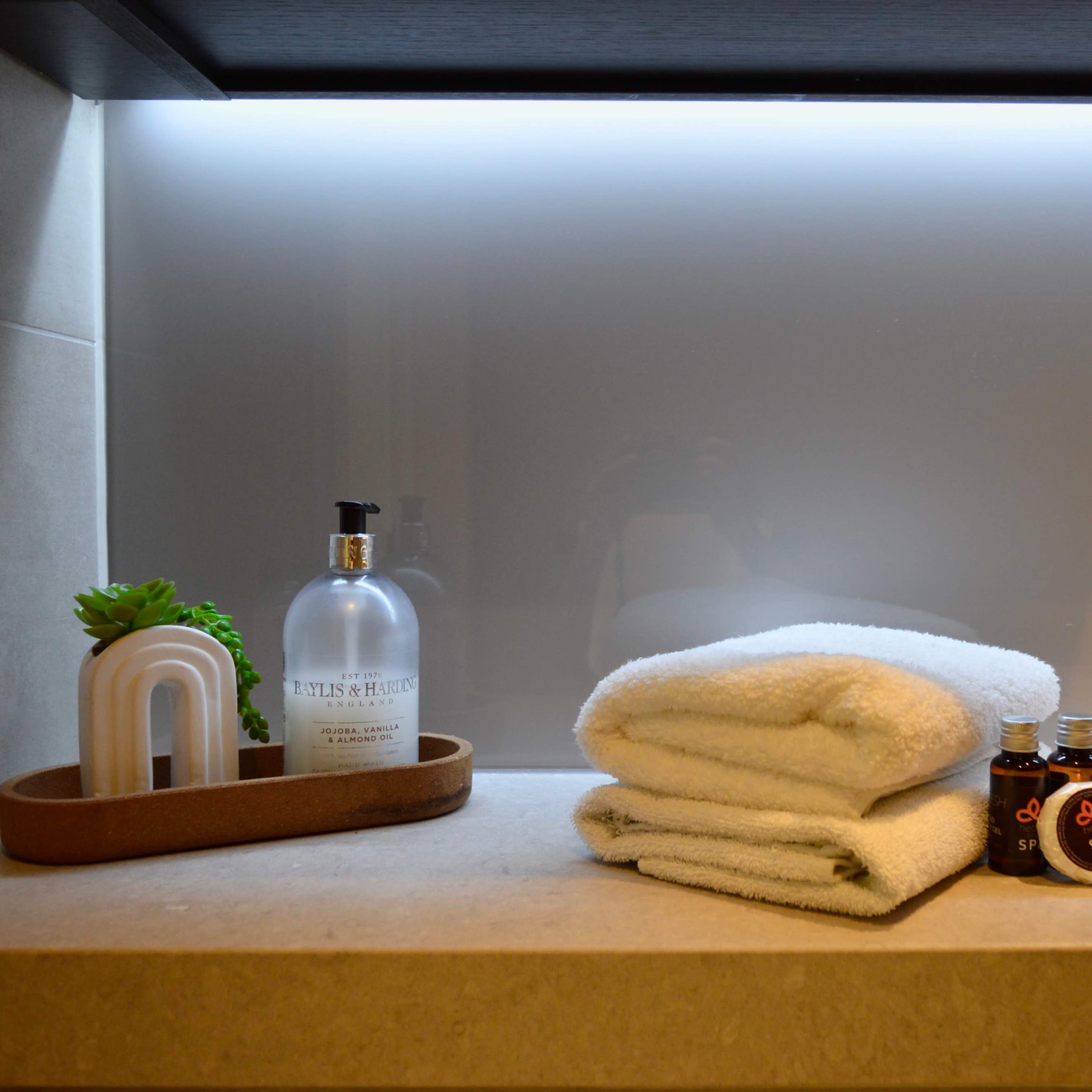 Neatly arranged white towels, a bottle of hand soap, a small plant, and decorative containers on a counter under soft lighting.