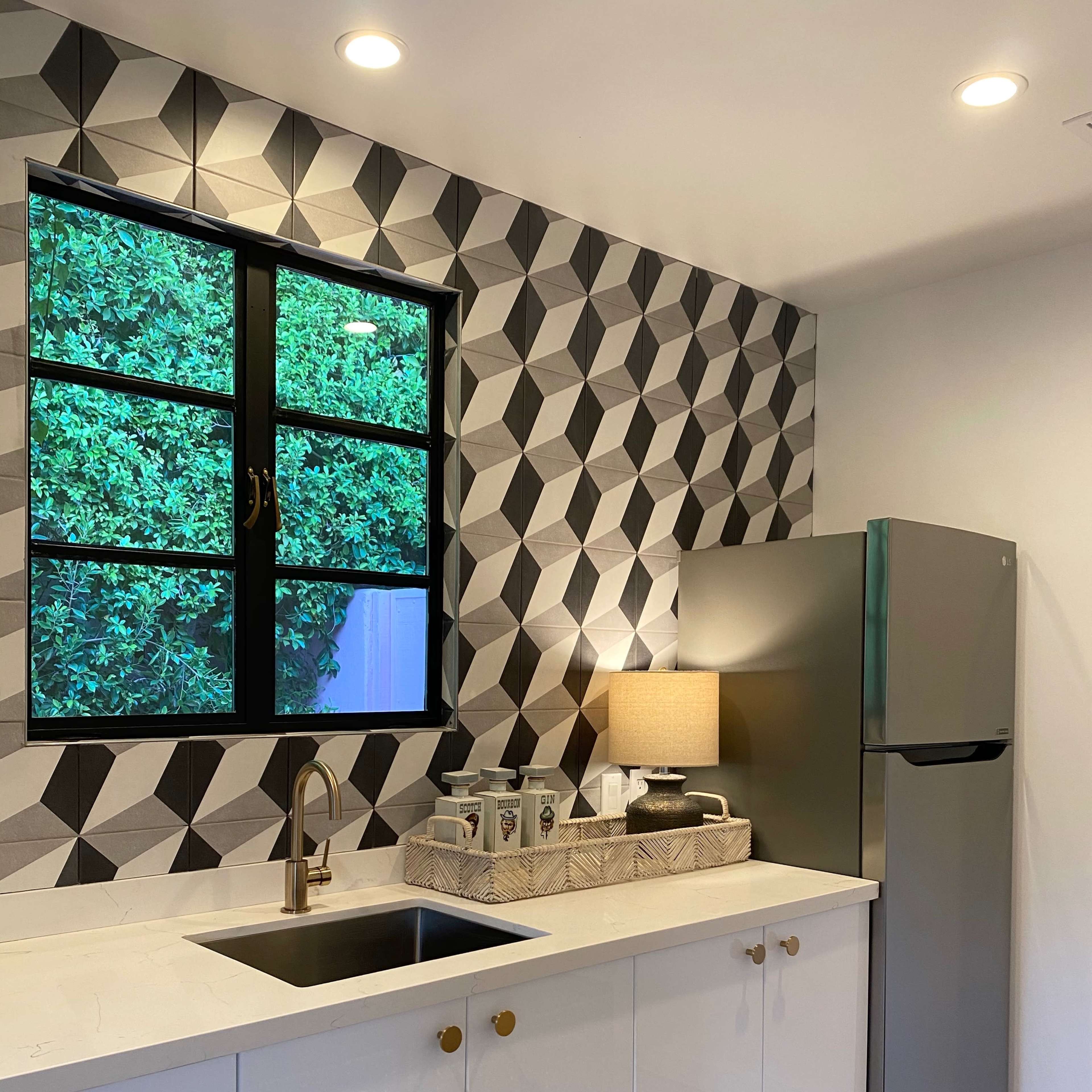 A modern kitchen features a geometric patterned wall, a stainless steel refrigerator, and a sink with a gold faucet.