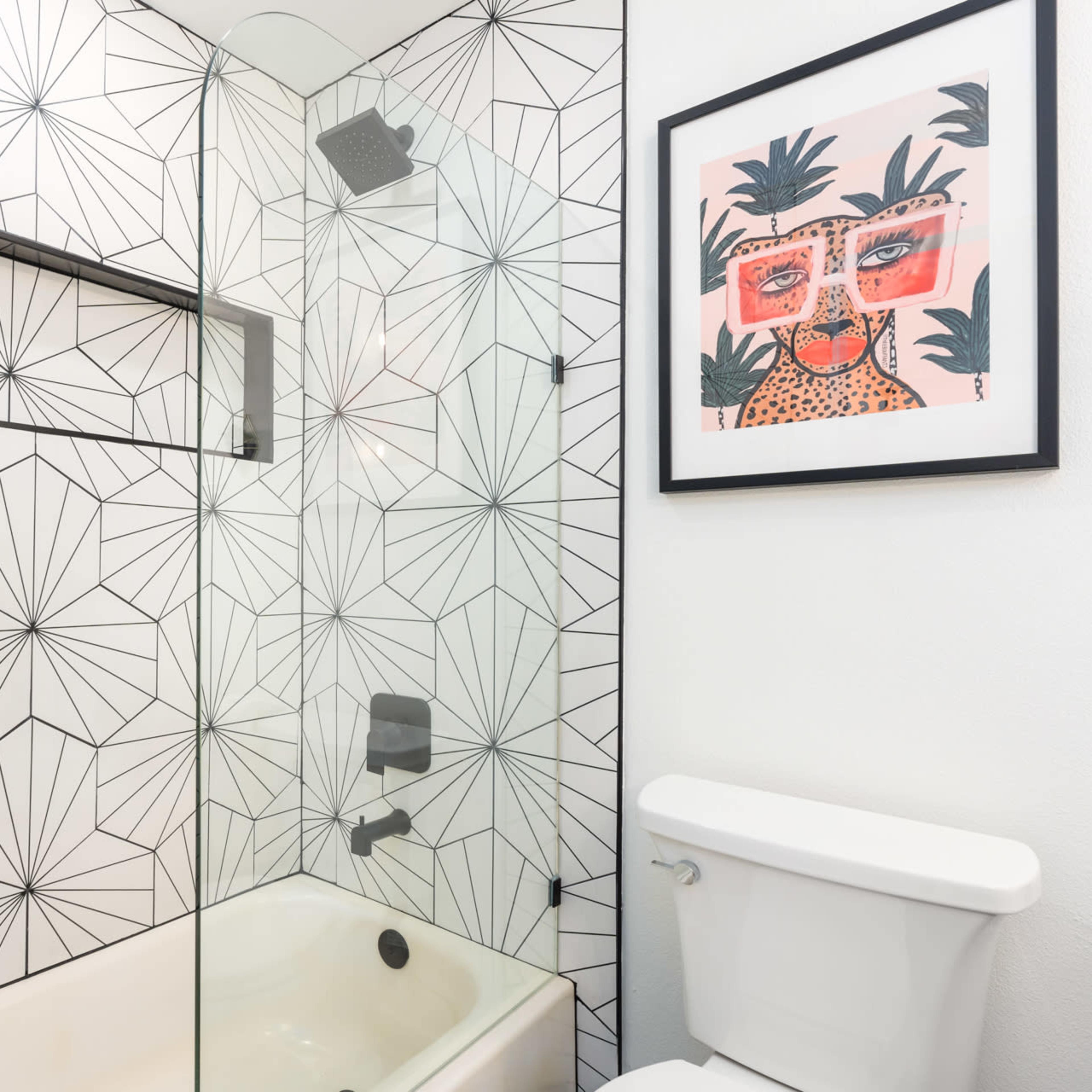 A modern bathroom featuring a glass-enclosed shower with geometric patterned tile walls, a bathtub, and a framed artwork on the wall.