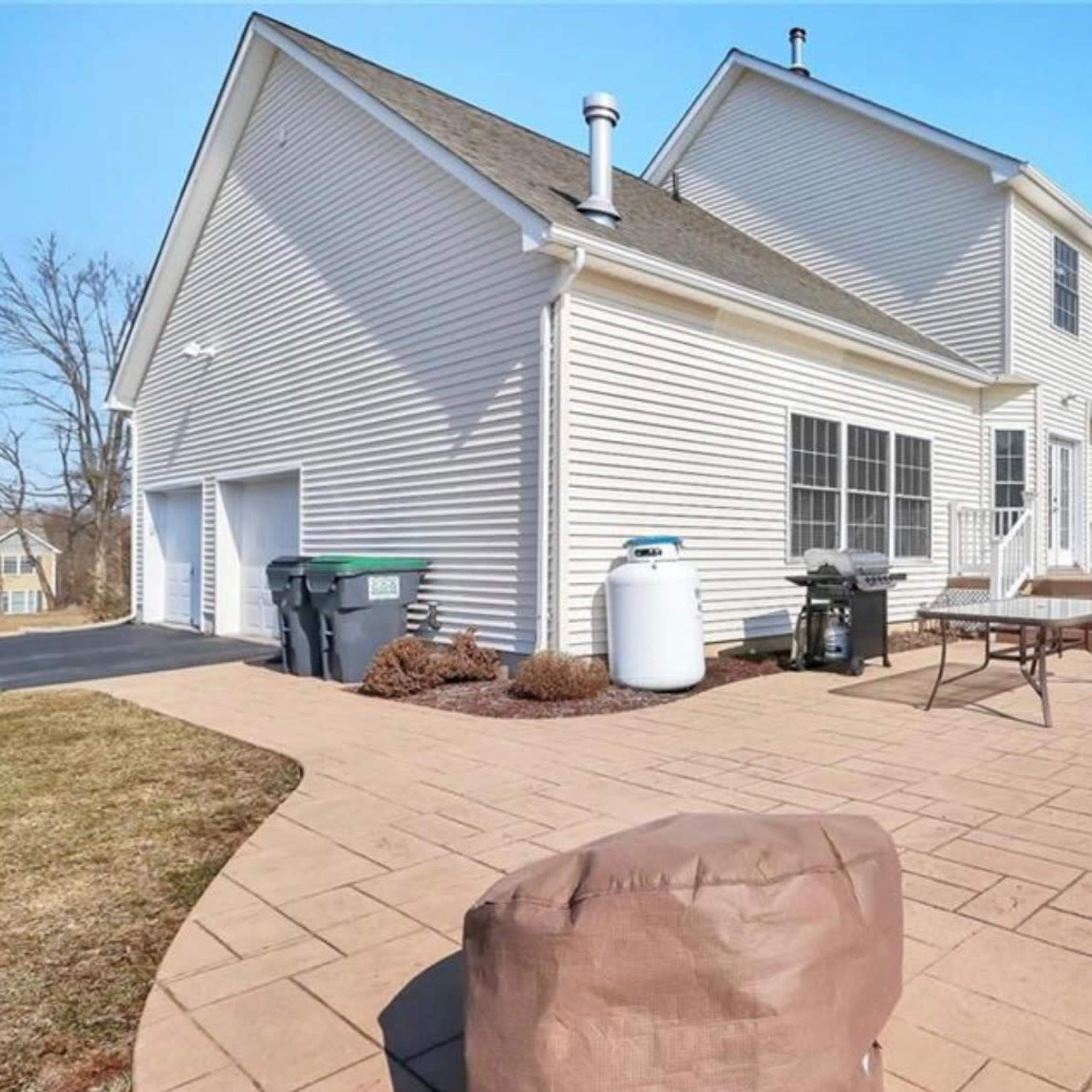 The rear exterior of a two-story house with a patio, green lawn, and outdoor furniture.