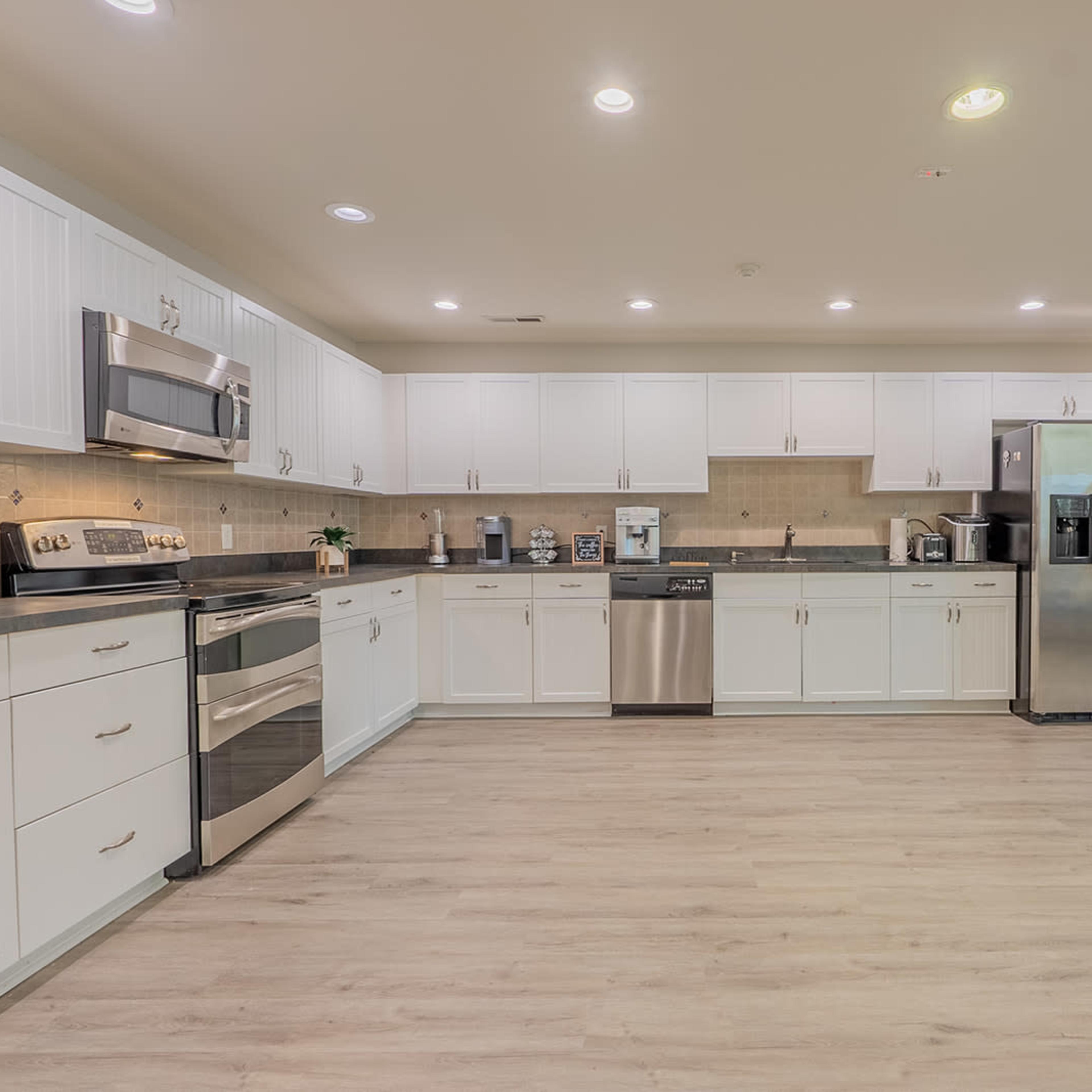 A modern kitchen features white cabinetry, stainless steel appliances, and a light wood floor.