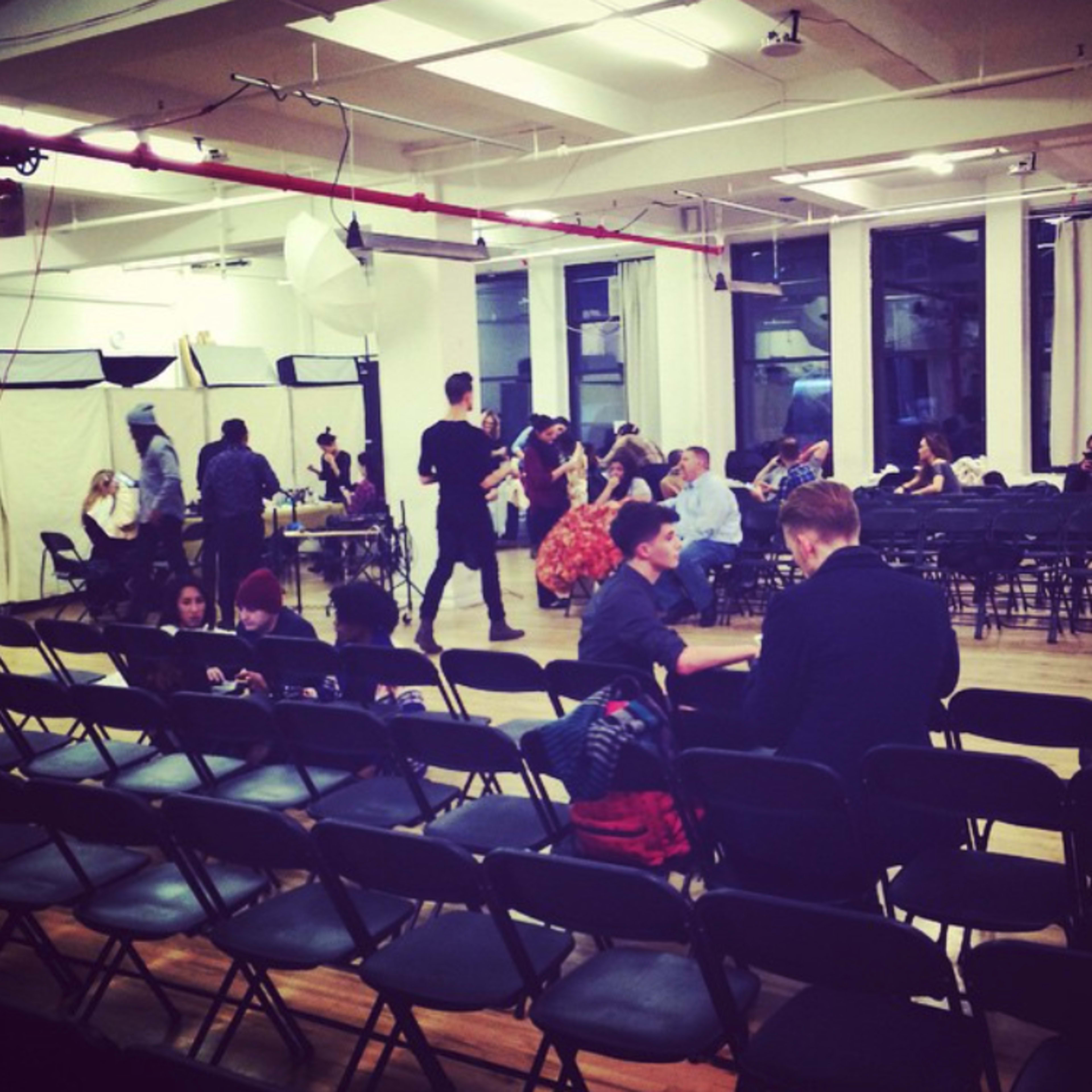 A spacious room with rows of empty chairs, where people are preparing for an event, while others are seated and interacting.