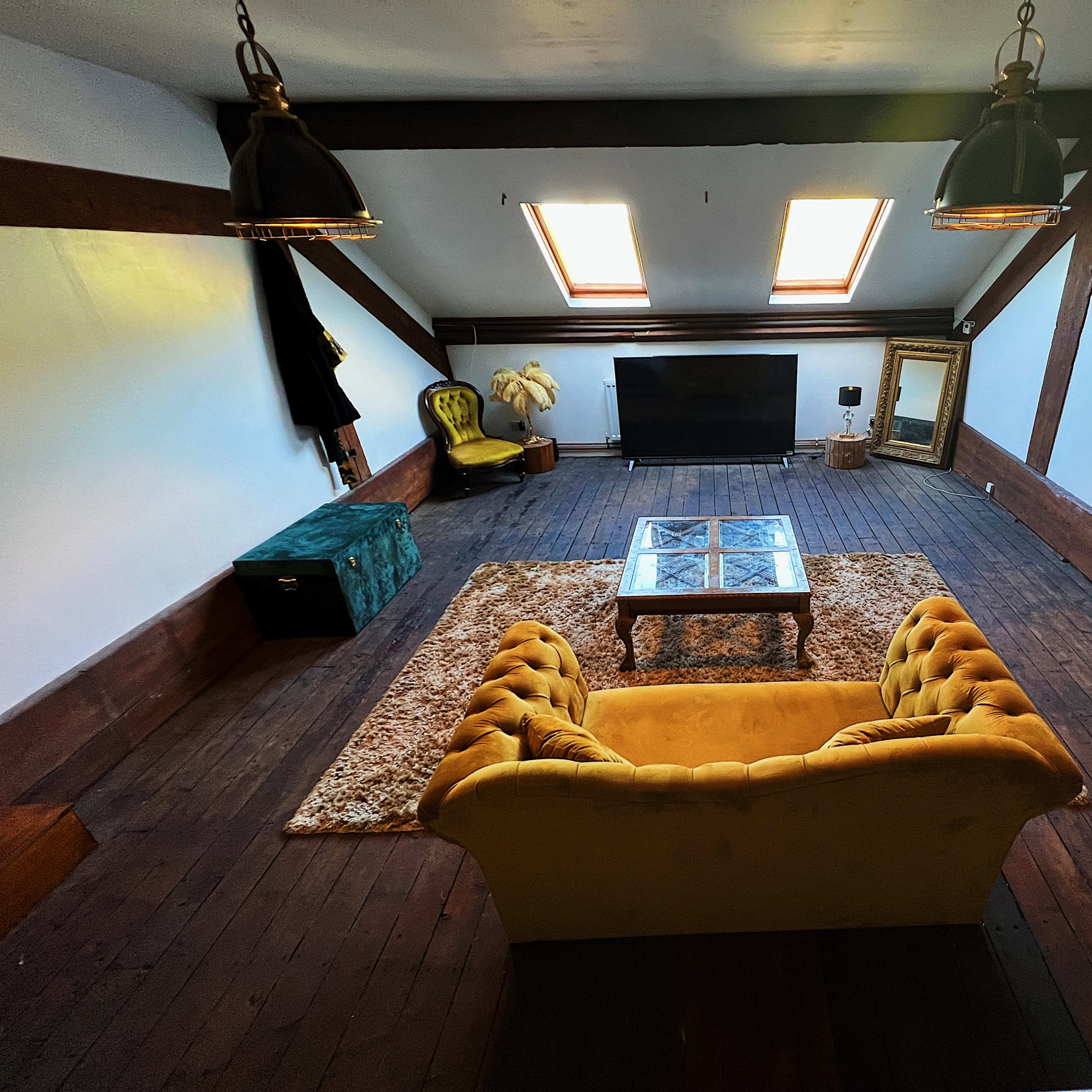 A spacious living area with a yellow couch, a glass coffee table, a television, and a couple of skylights illuminating the wooden floor.