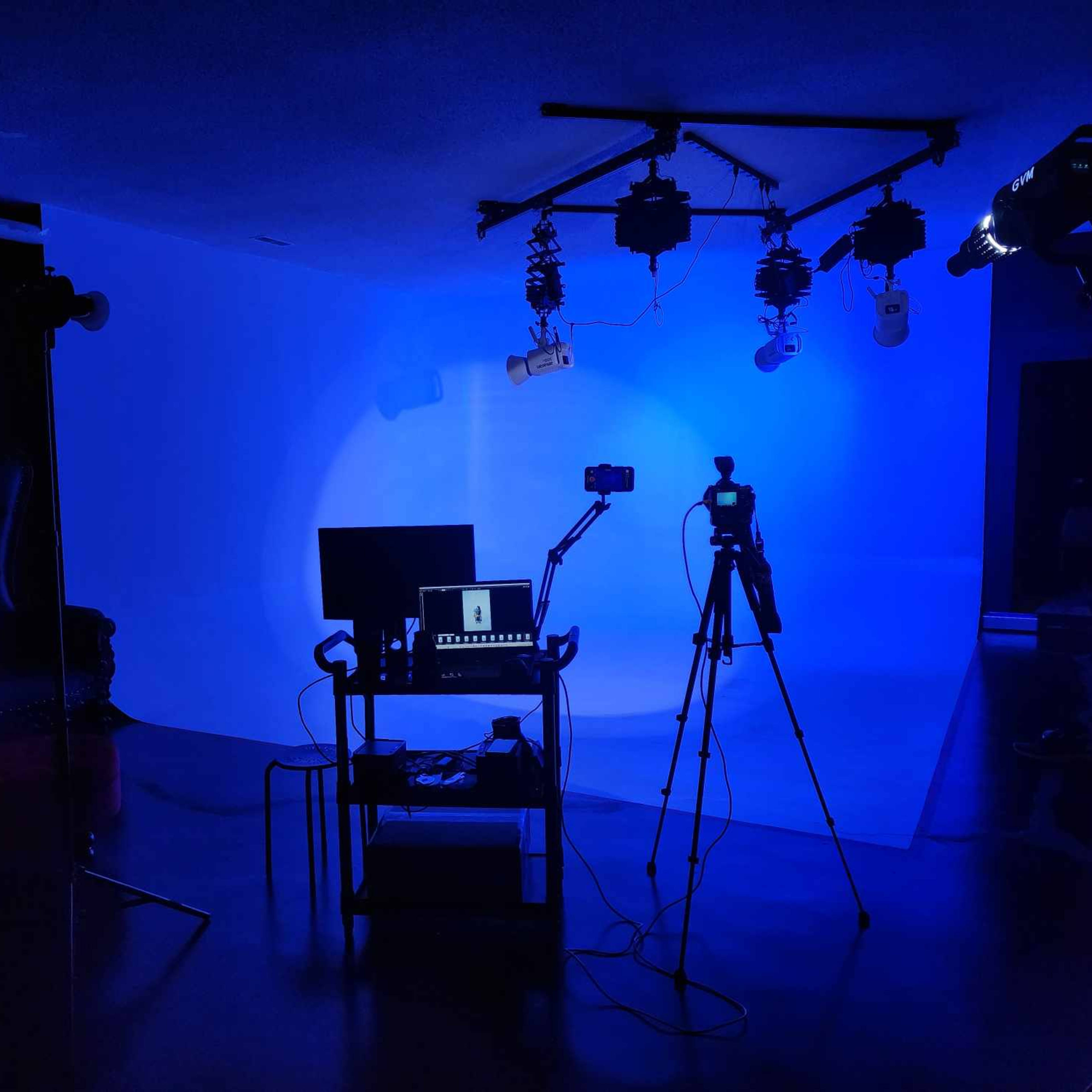 A dimly lit studio setup with a blue backdrop, a table with equipment, and two cameras on tripods.