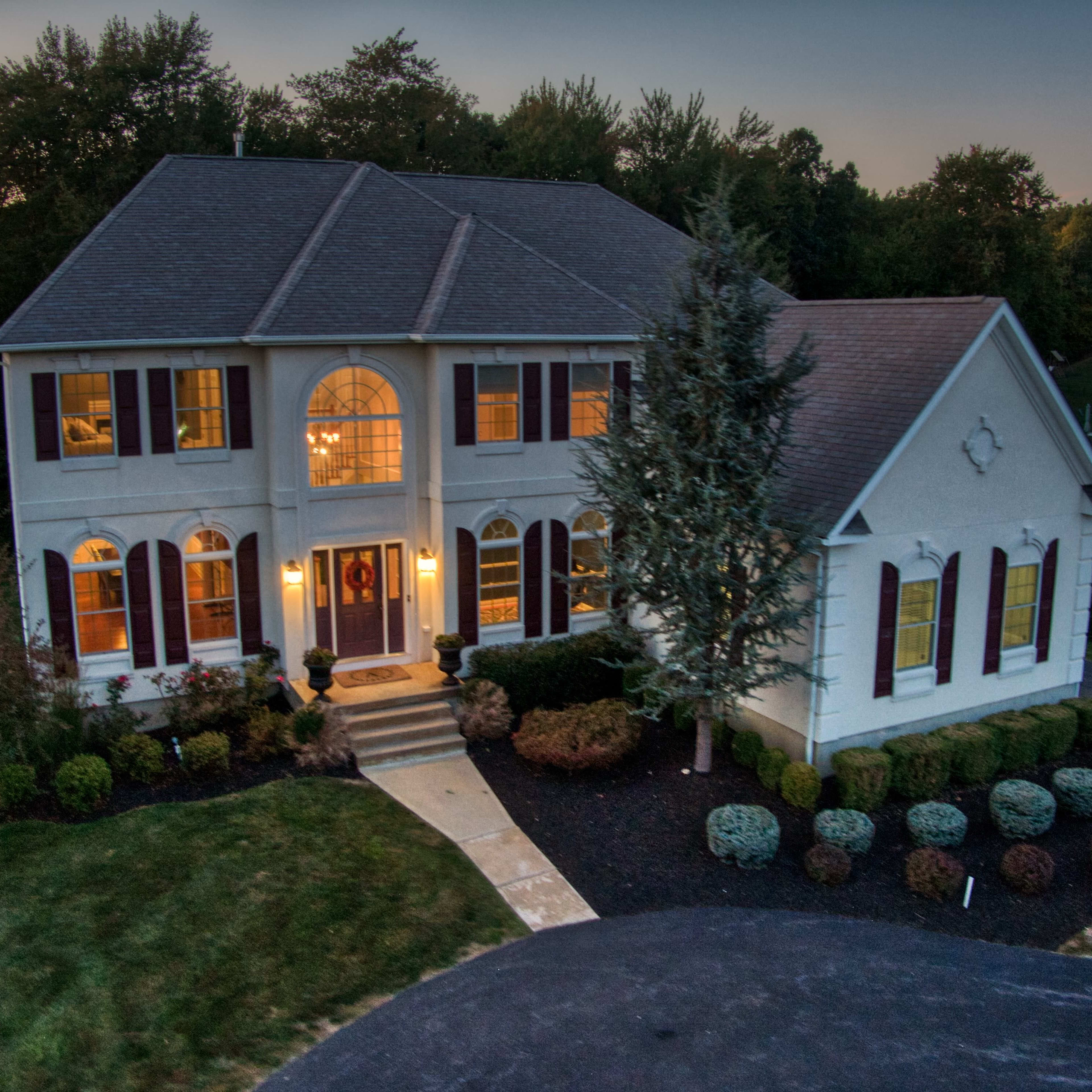 A large, two-story house with a symmetrical facade, surrounded by landscaped greenery and a stone pathway leading to the front entrance.