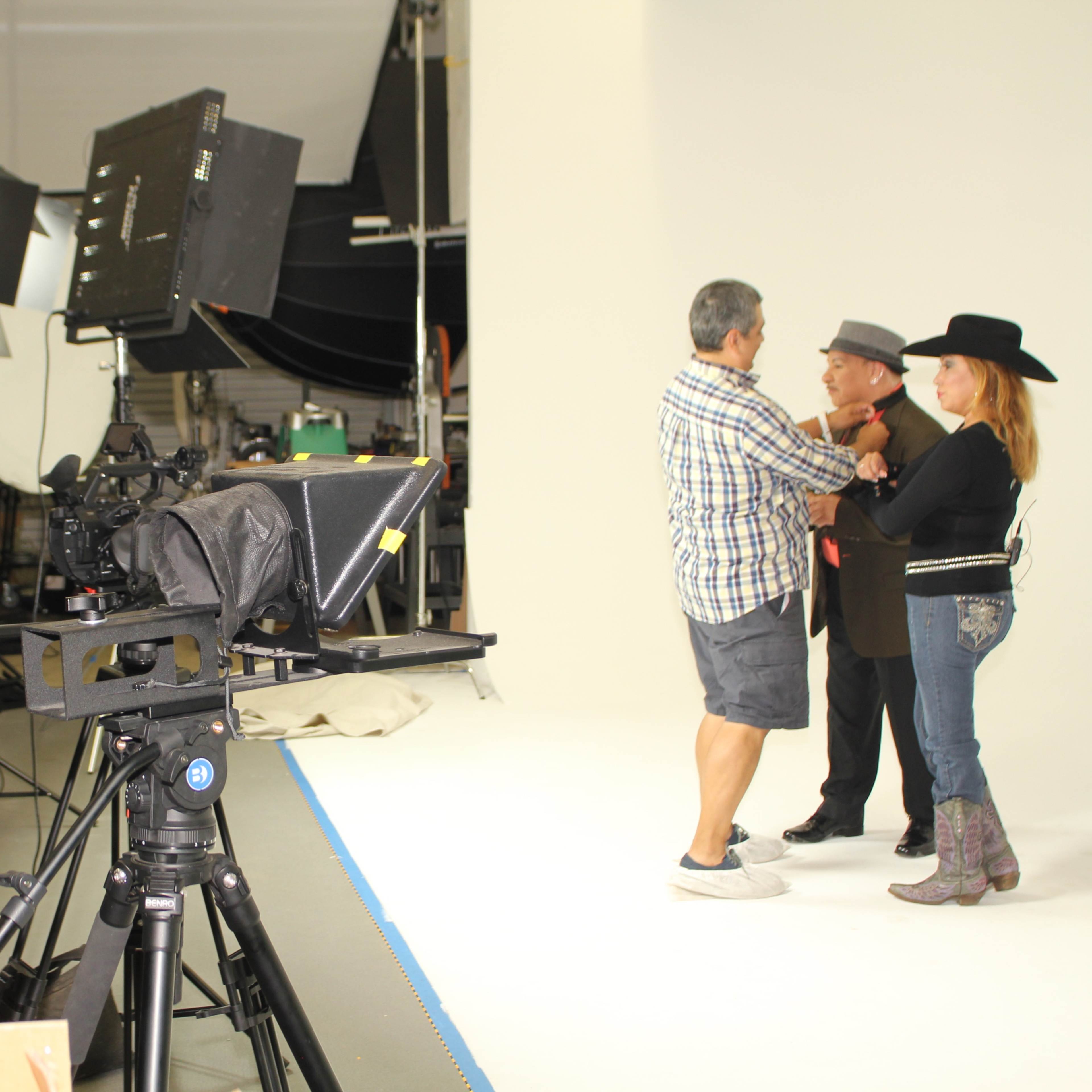 A film production set features a crew preparing for a shoot with two actors interacting in front of a backdrop and lighting equipment.
