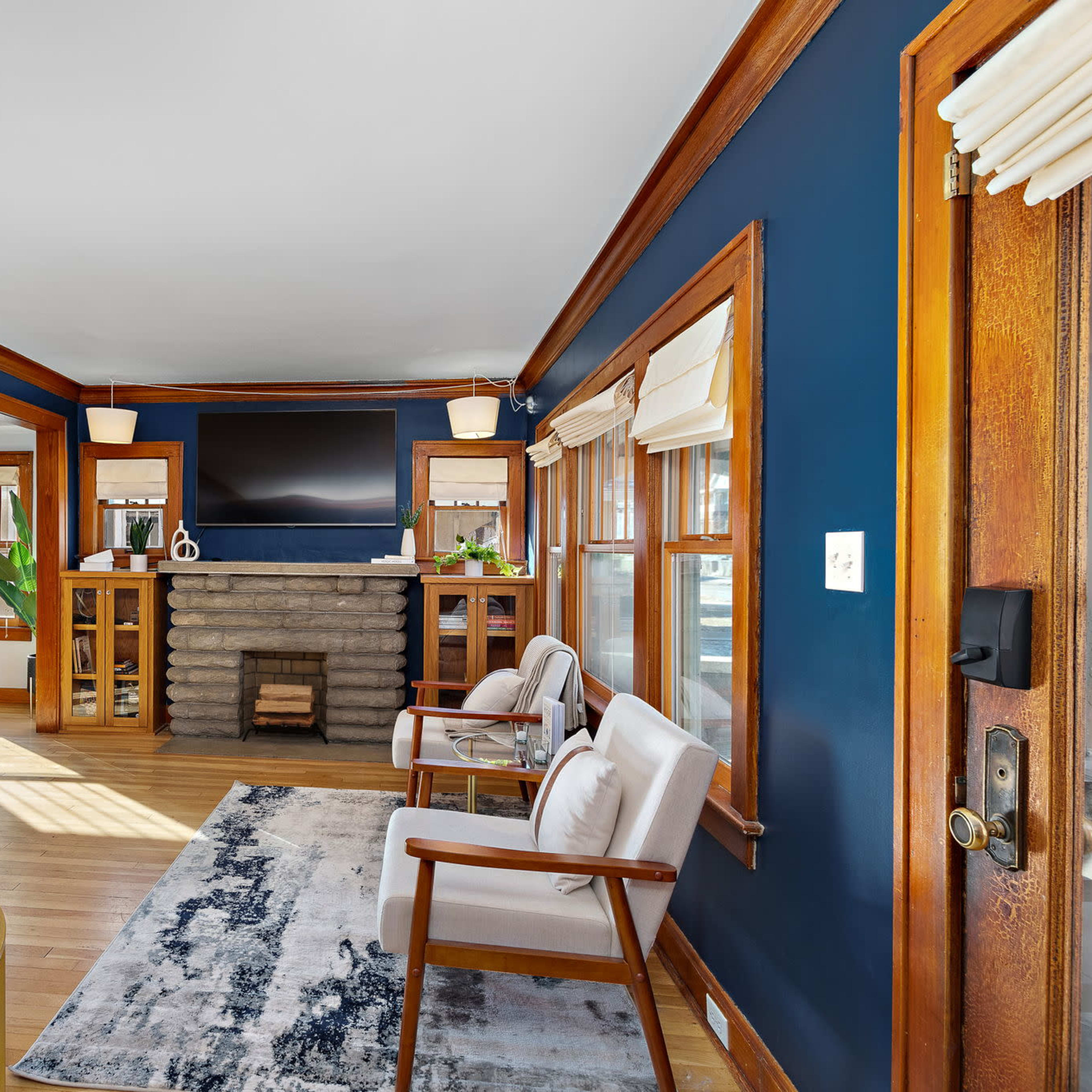 A room with dark blue walls, wooden trim, a stone fireplace, and two white armchairs arranged near a glass coffee table.
