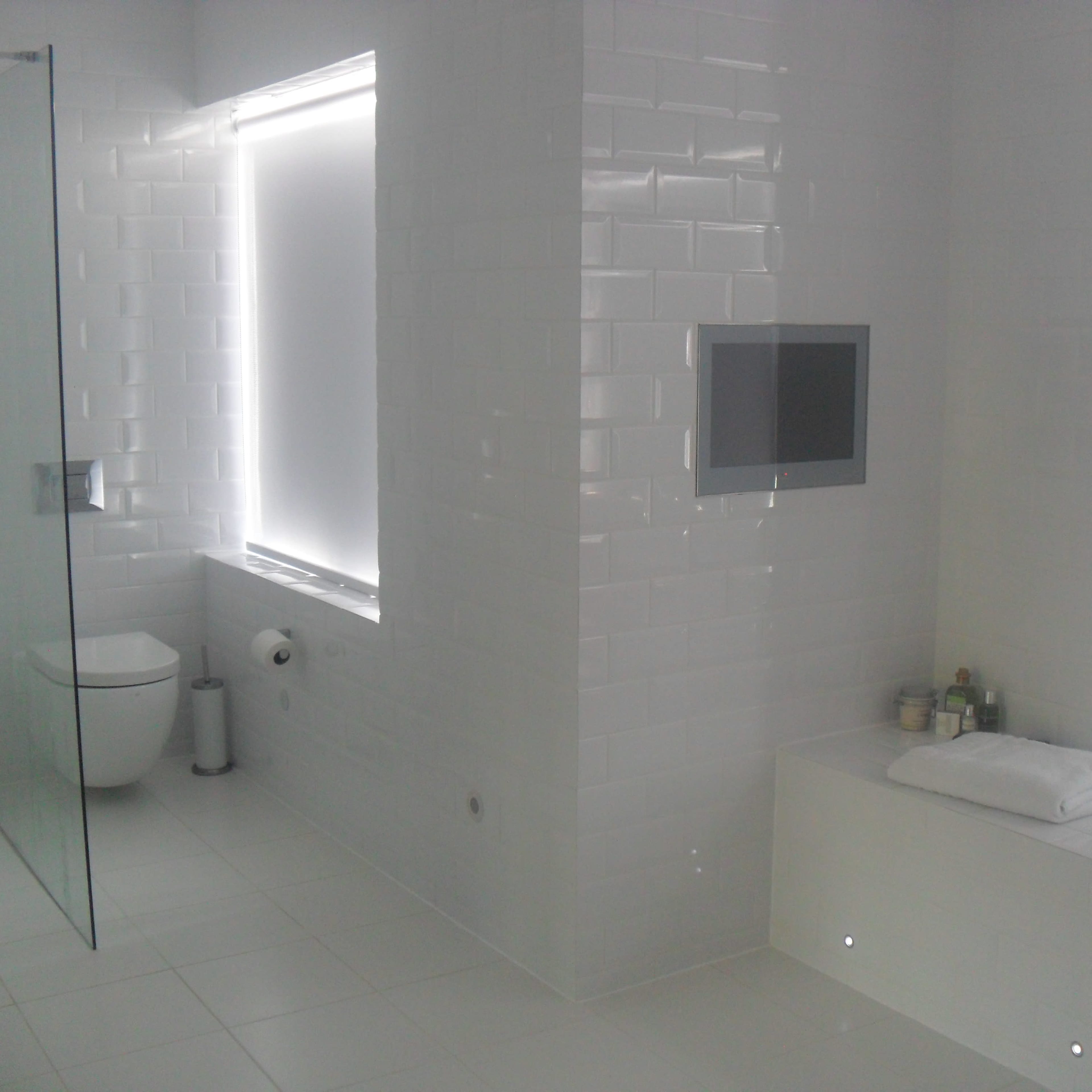 A contemporary bathroom with white tiled walls, a glass shower enclosure, a toilet, and a bathtub with minimalist decor.