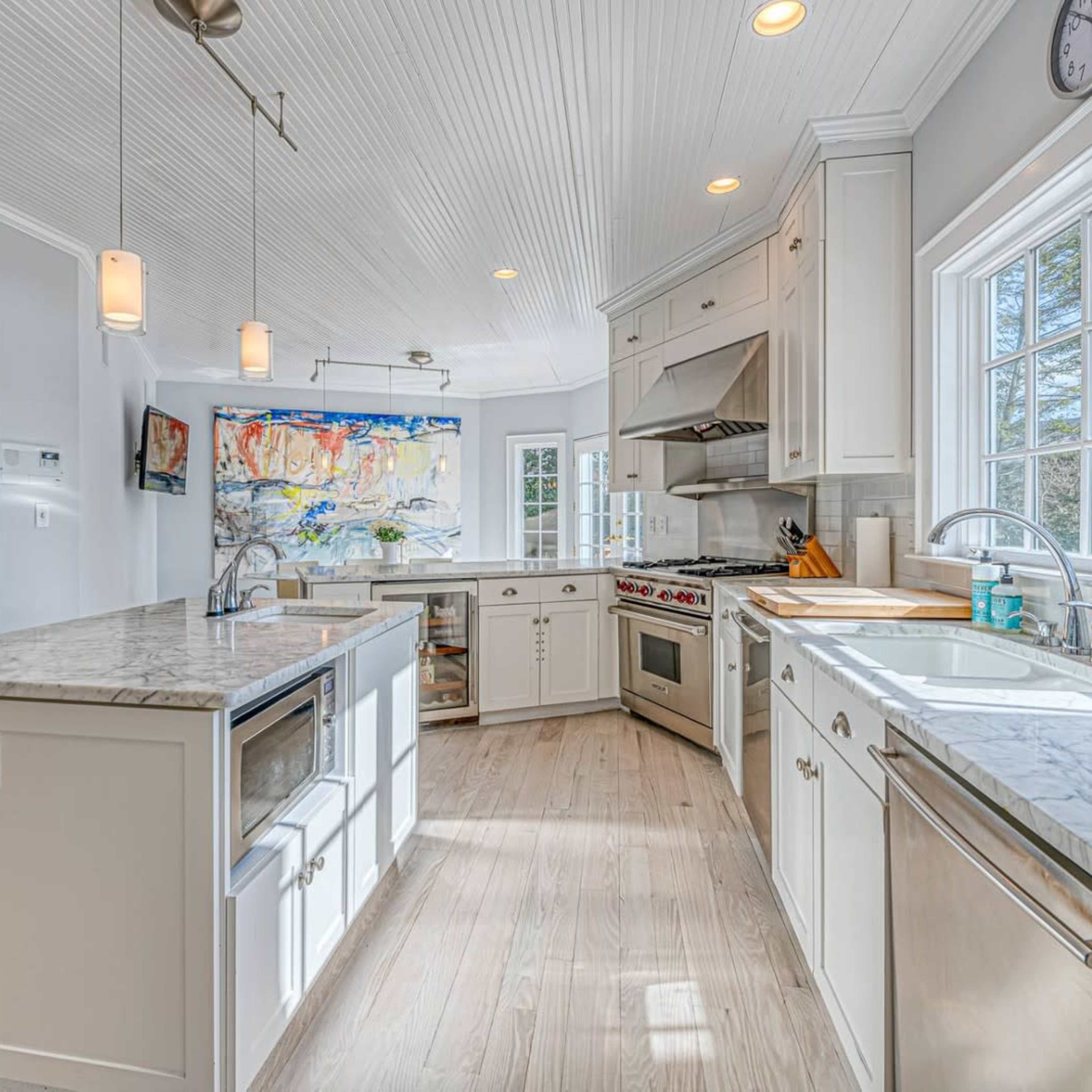 The kitchen features white cabinetry, marble countertops, and stainless steel appliances, with large windows allowing natural light to fill the space.