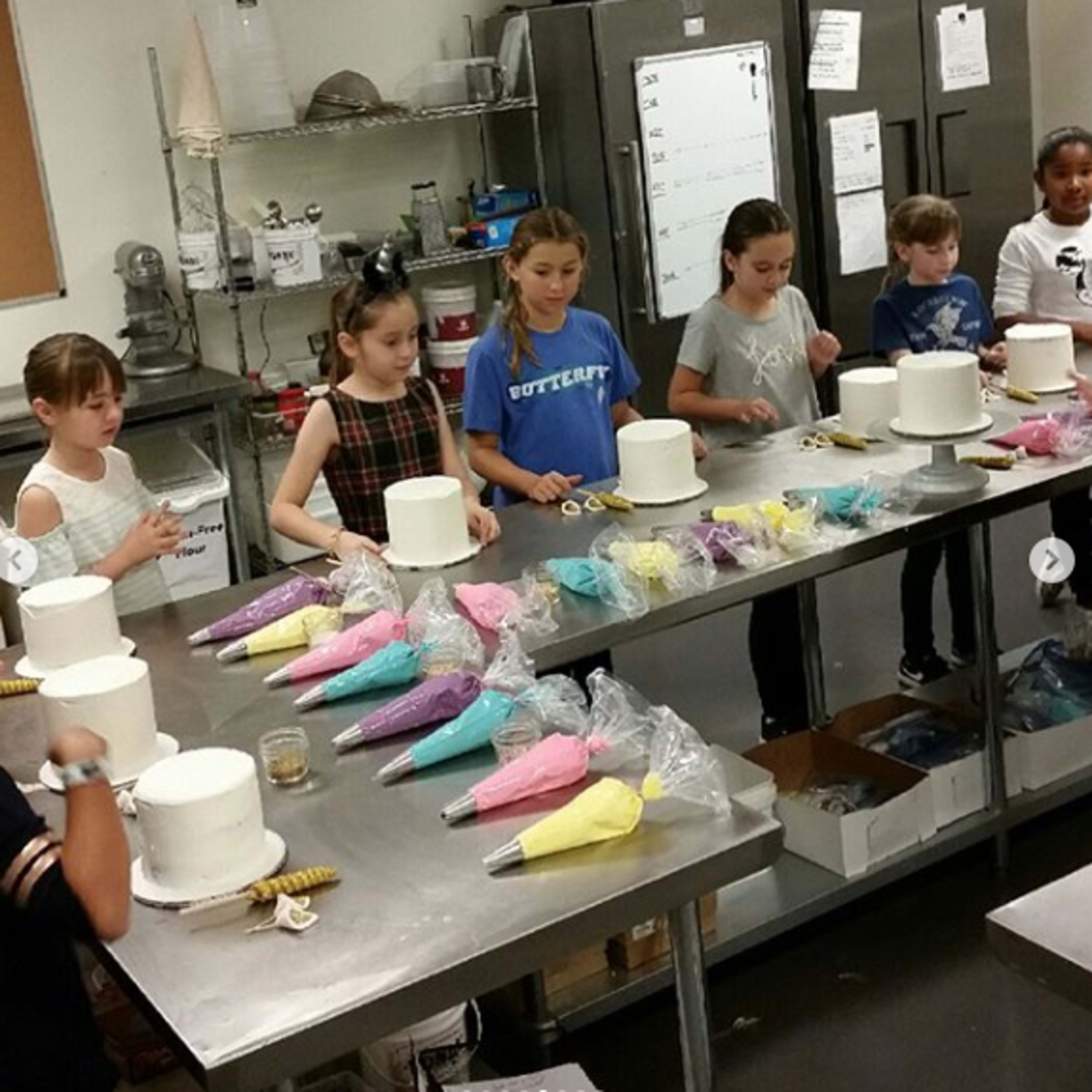 A group of children is decorating white cakes with colorful icing in a kitchen setting.