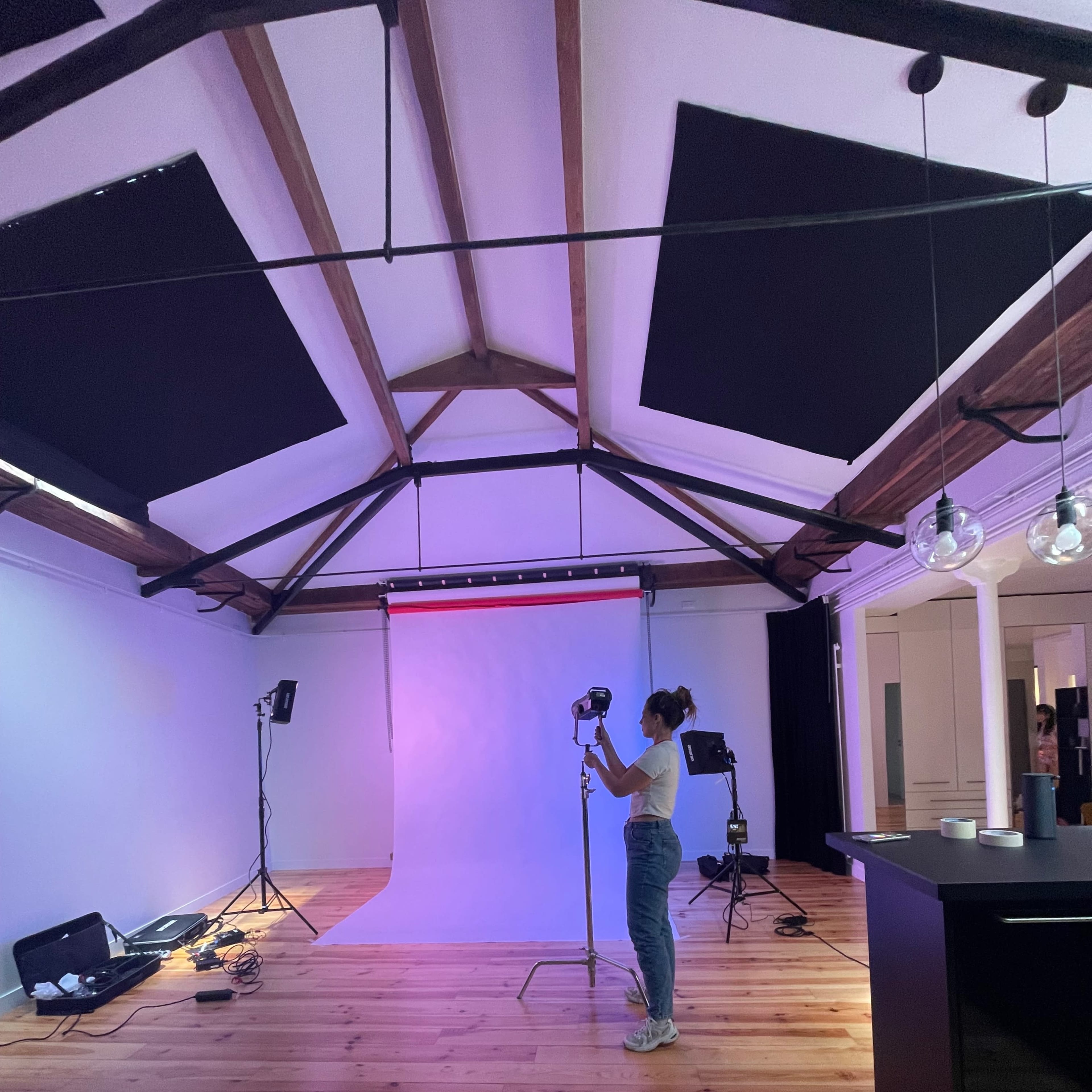 A person stands in a spacious studio with a light setup and a backdrop, preparing for a photoshoot.
