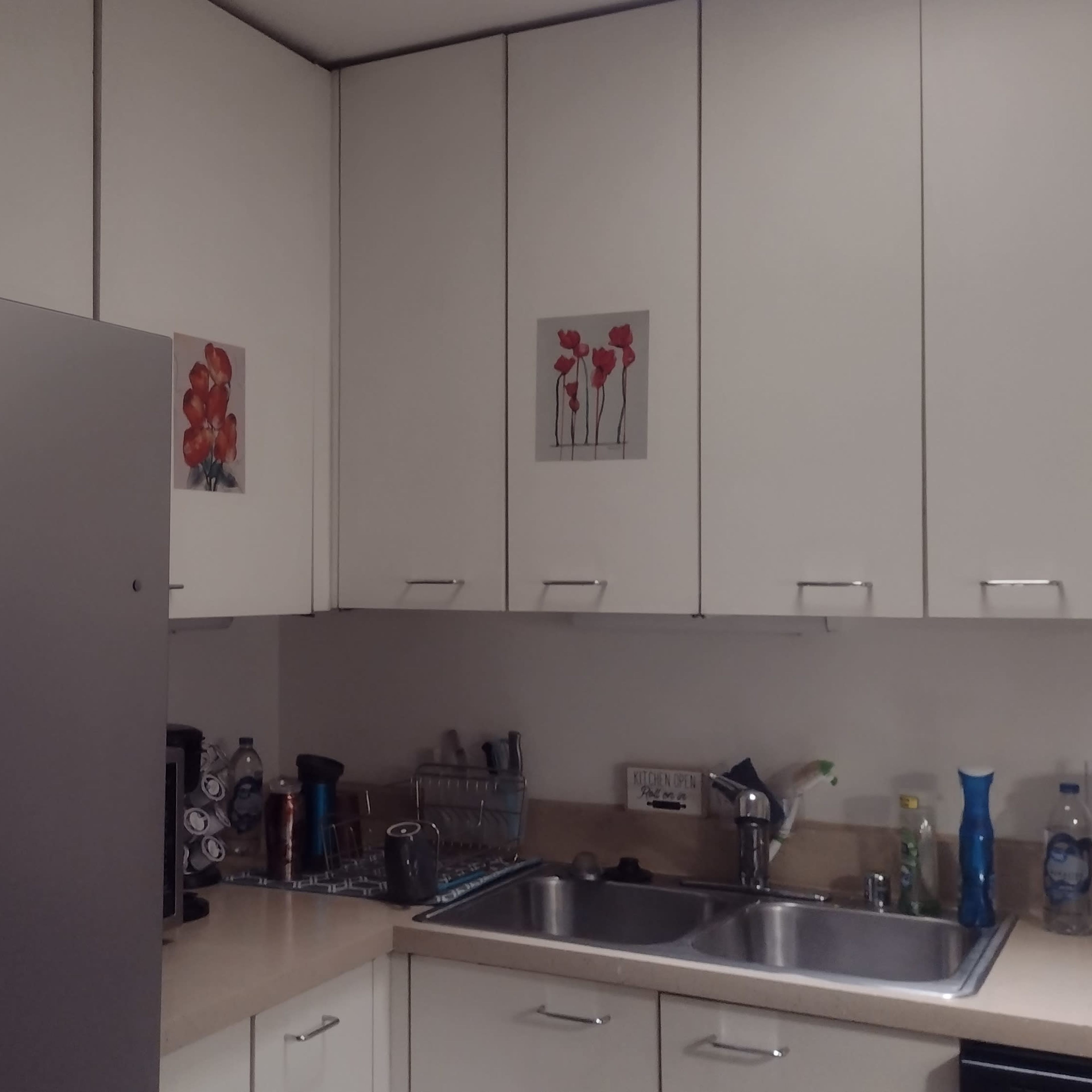 A modern kitchen with white cabinets, a stainless steel refrigerator, a sink, and various kitchenware on the counter.