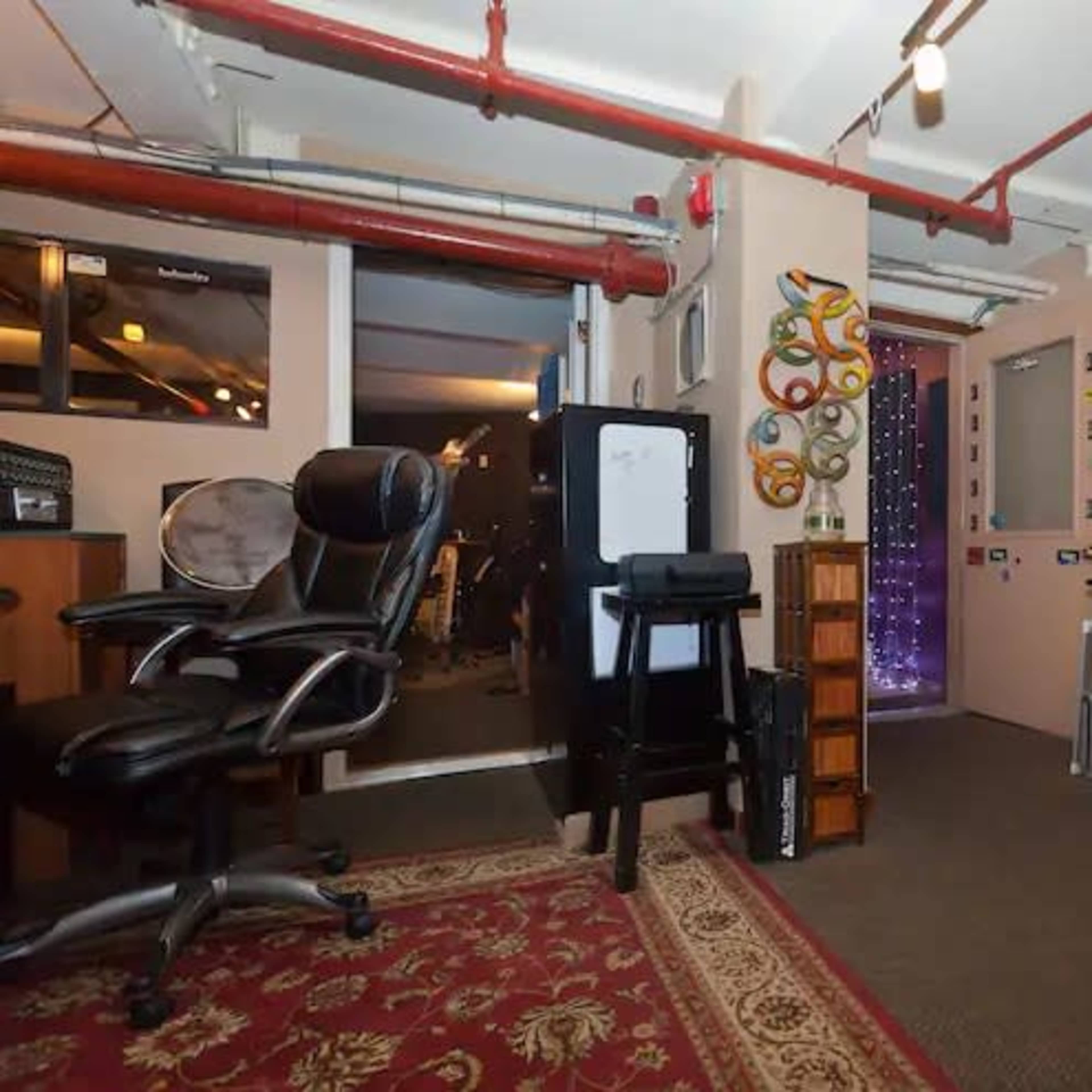 An office space with two black chairs, a wooden cabinet, and various items on the walls, including decorative pieces and a standing keyboard.
