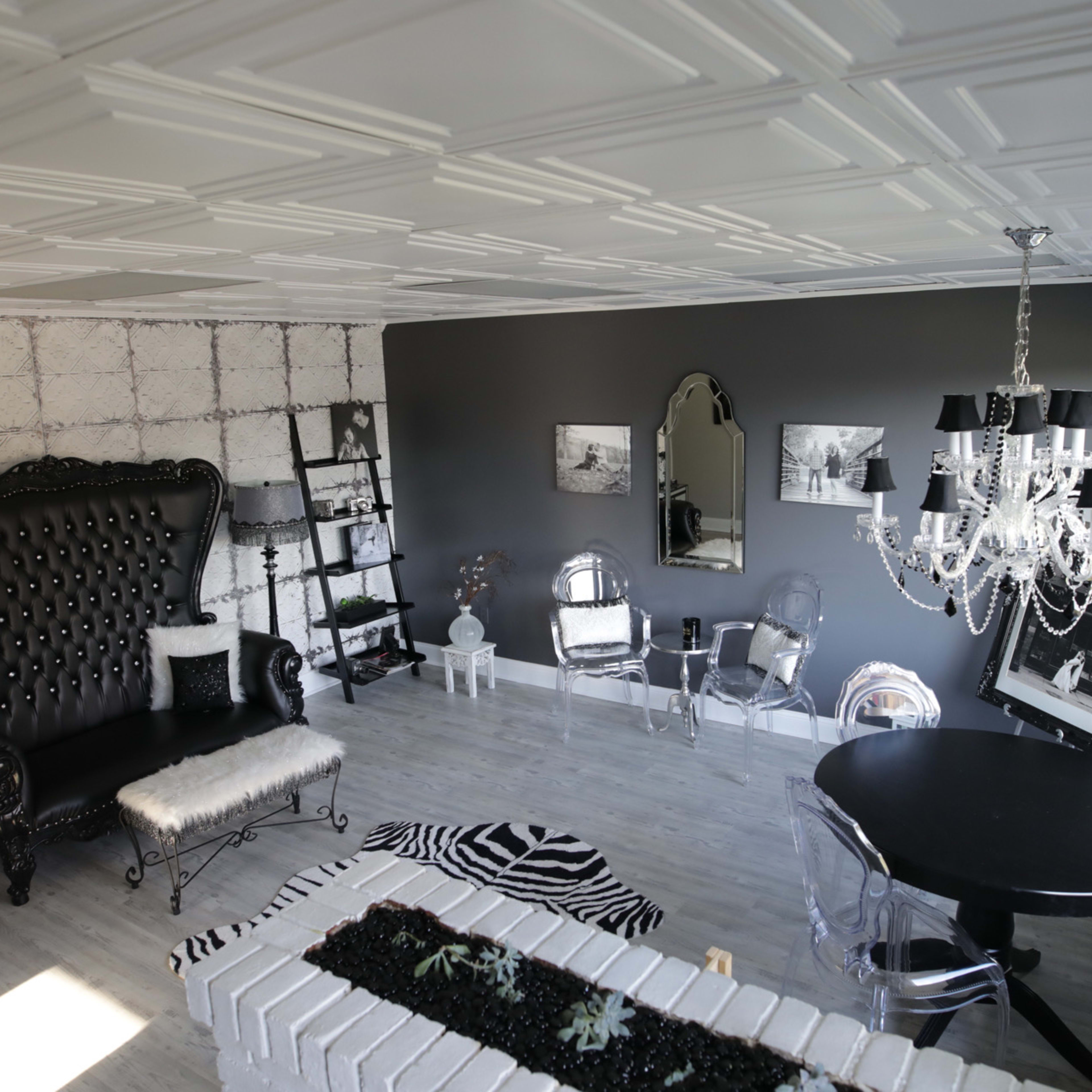 A modern living room featuring a large black tufted sofa, a round black dining table, and a chandelier, with a mix of decorative elements on the walls and floor.