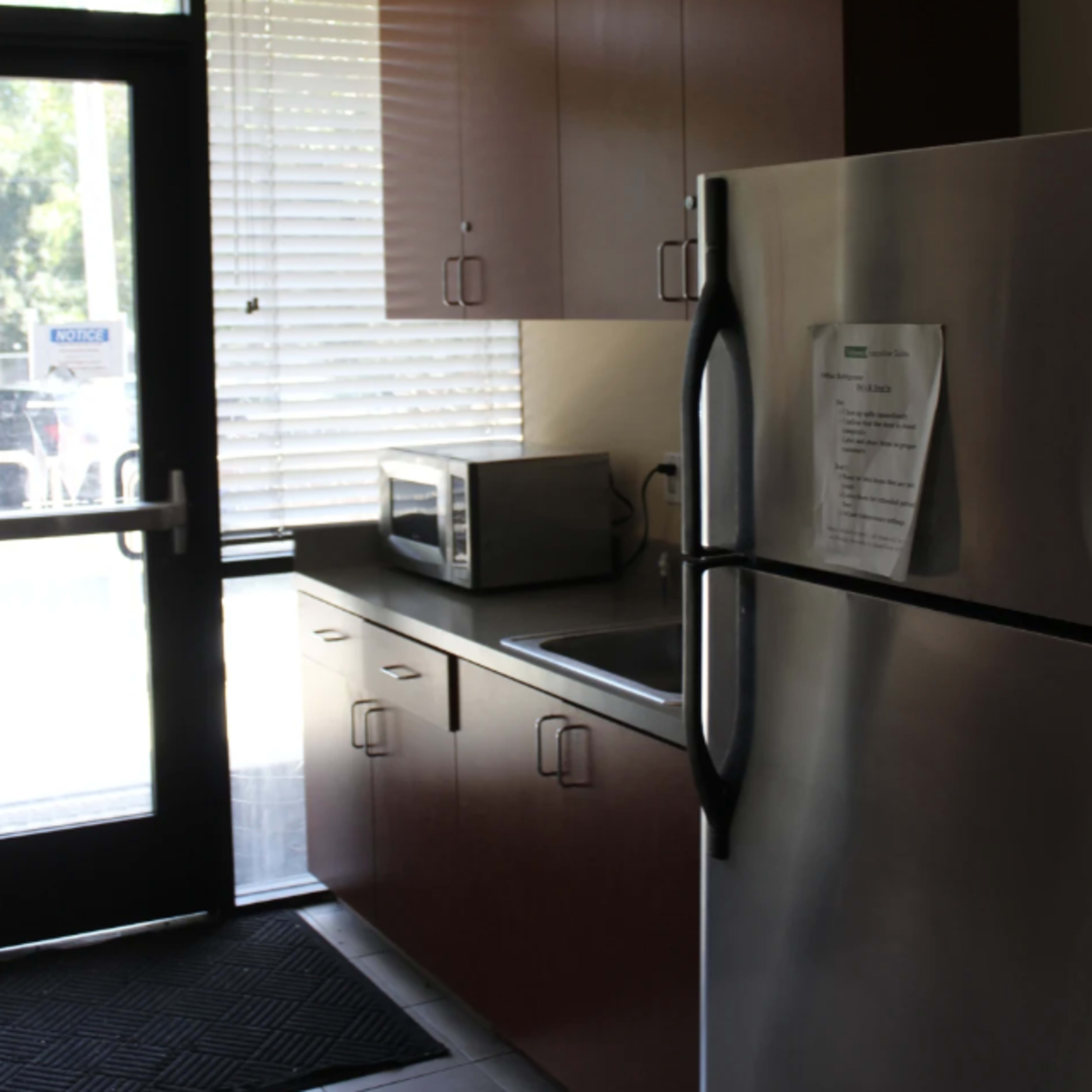 A kitchen area with wooden cabinets, a stainless steel refrigerator, a microwave, and a doorway leading outside.