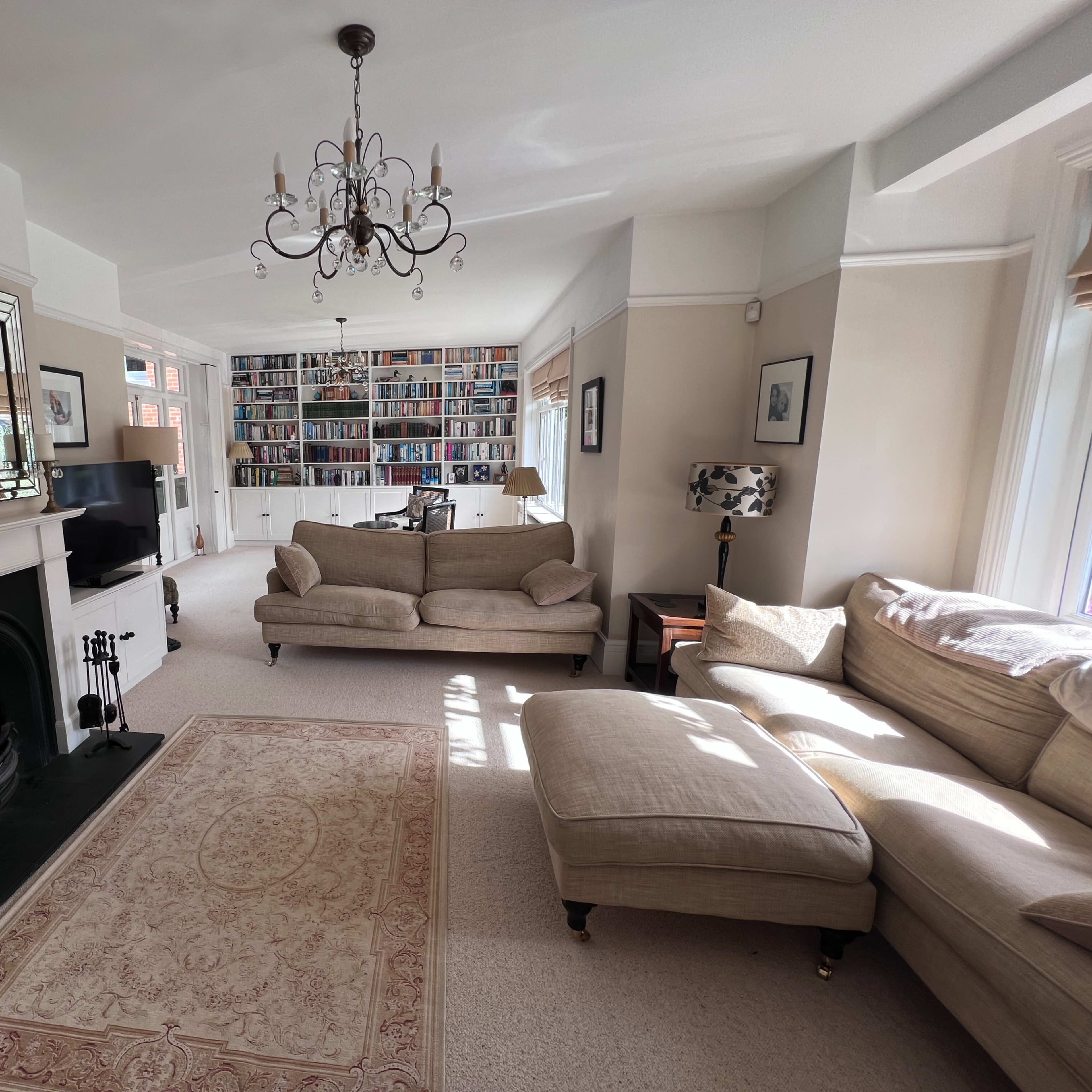 A spacious living room features a large bookshelf filled with books, a chandelier, a fireplace, and multiple seating areas.