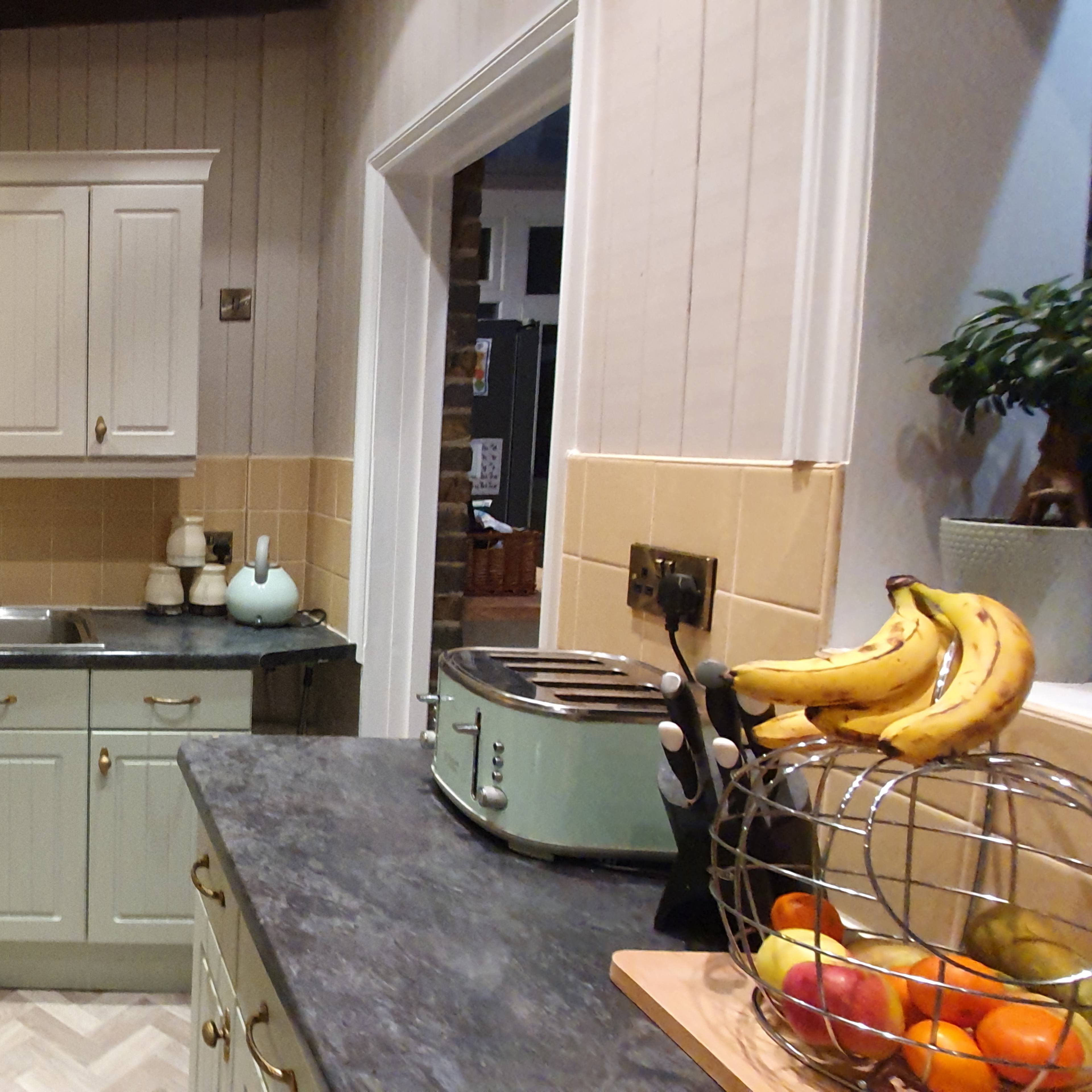 A modern kitchen with light-colored cabinets, a stainless steel sink, and a counter filled with a fruit basket and kitchen appliances.