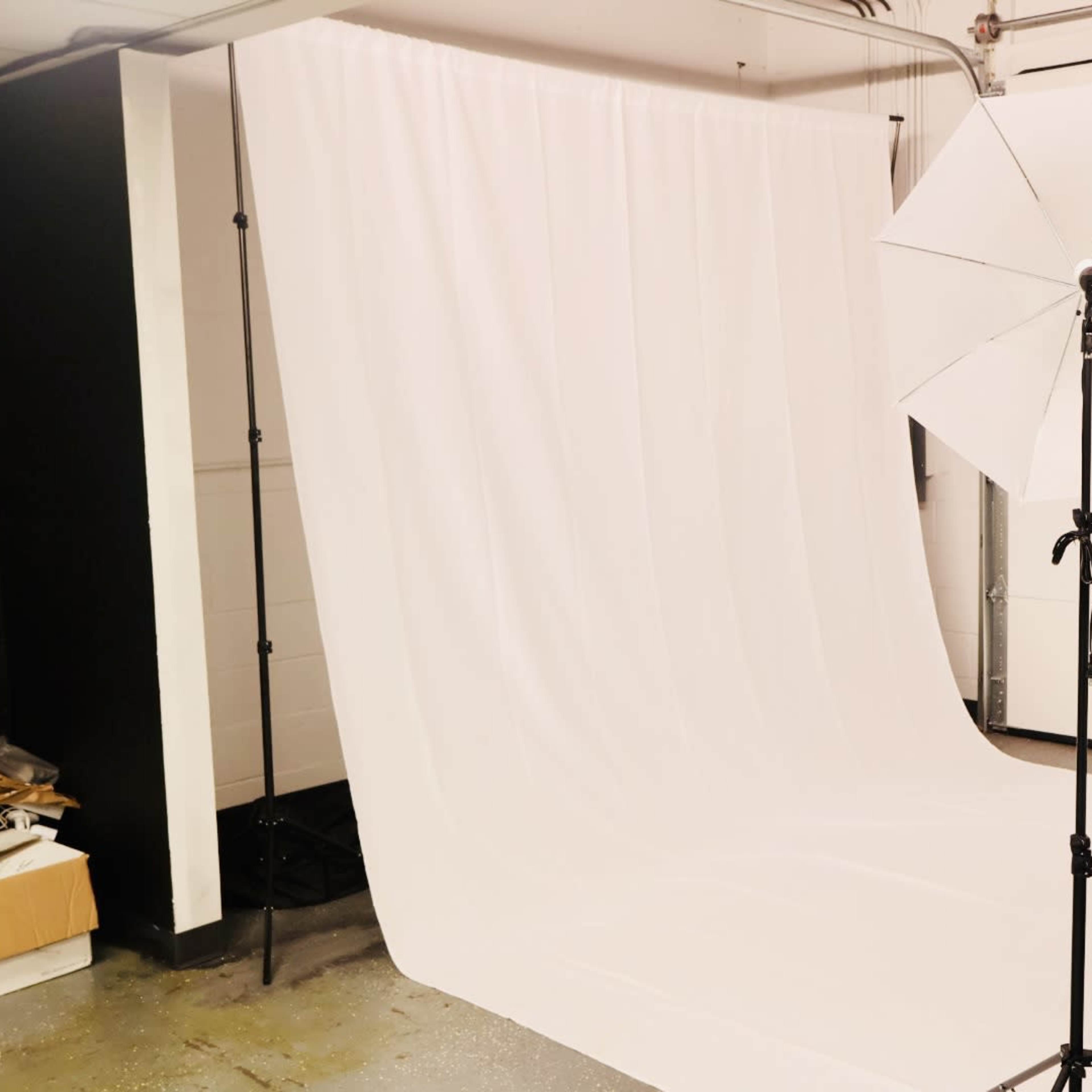 A photography studio setup with a white backdrop and lighting equipment arranged in a garage space.