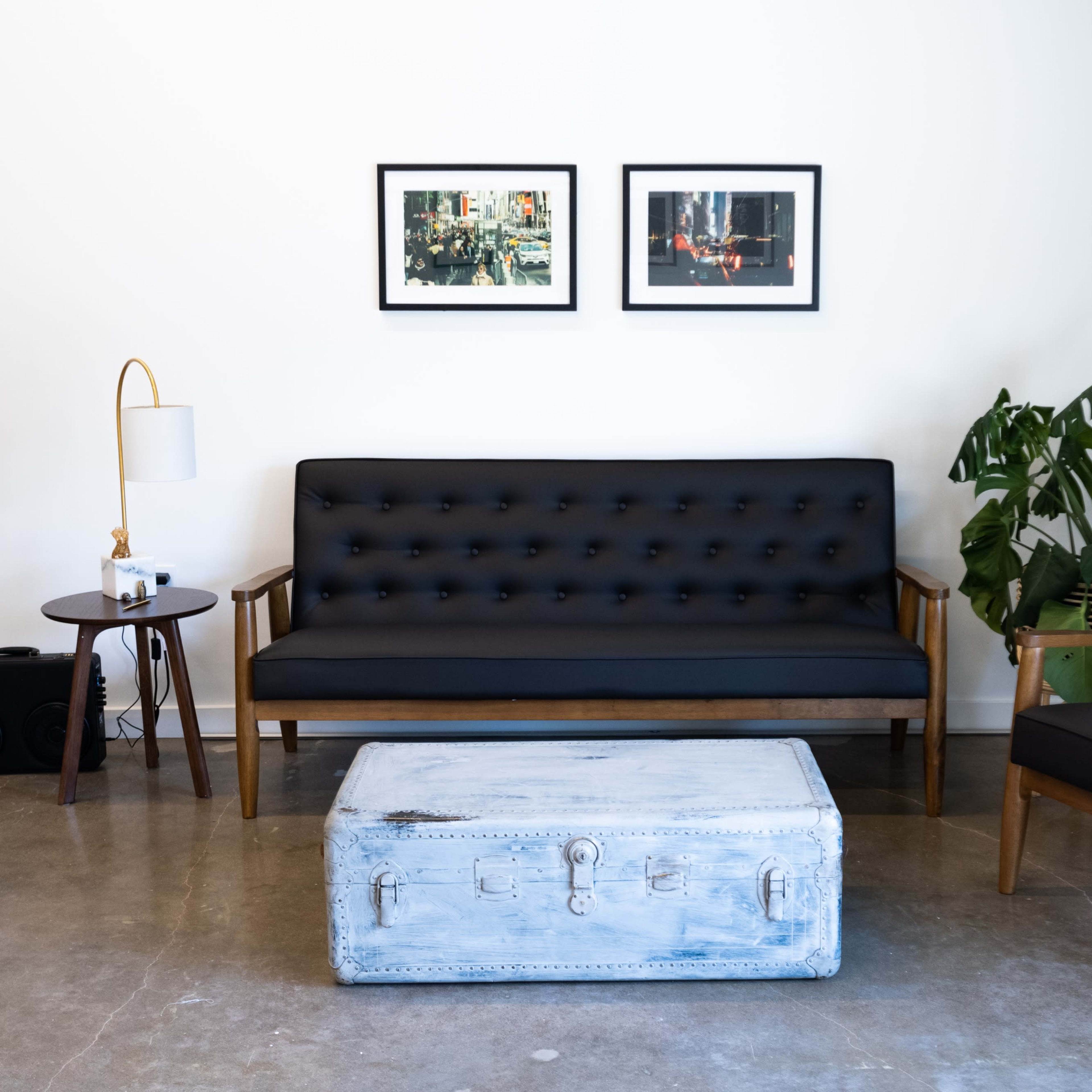 A minimalist living room with a black sofa, an armchair, a wooden coffee table, framed pictures on the wall, and a potted plant.
