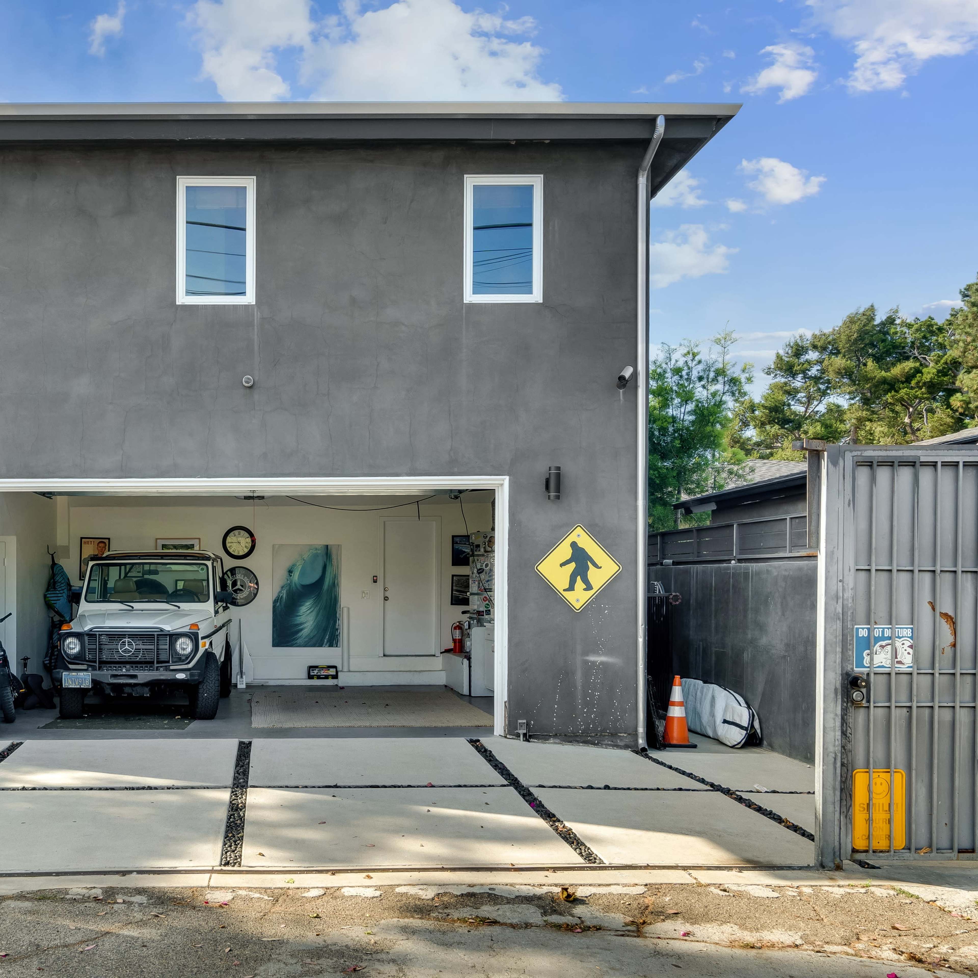 A two-story gray building with a large open garage displaying a vintage truck and a pedestrian crossing sign.