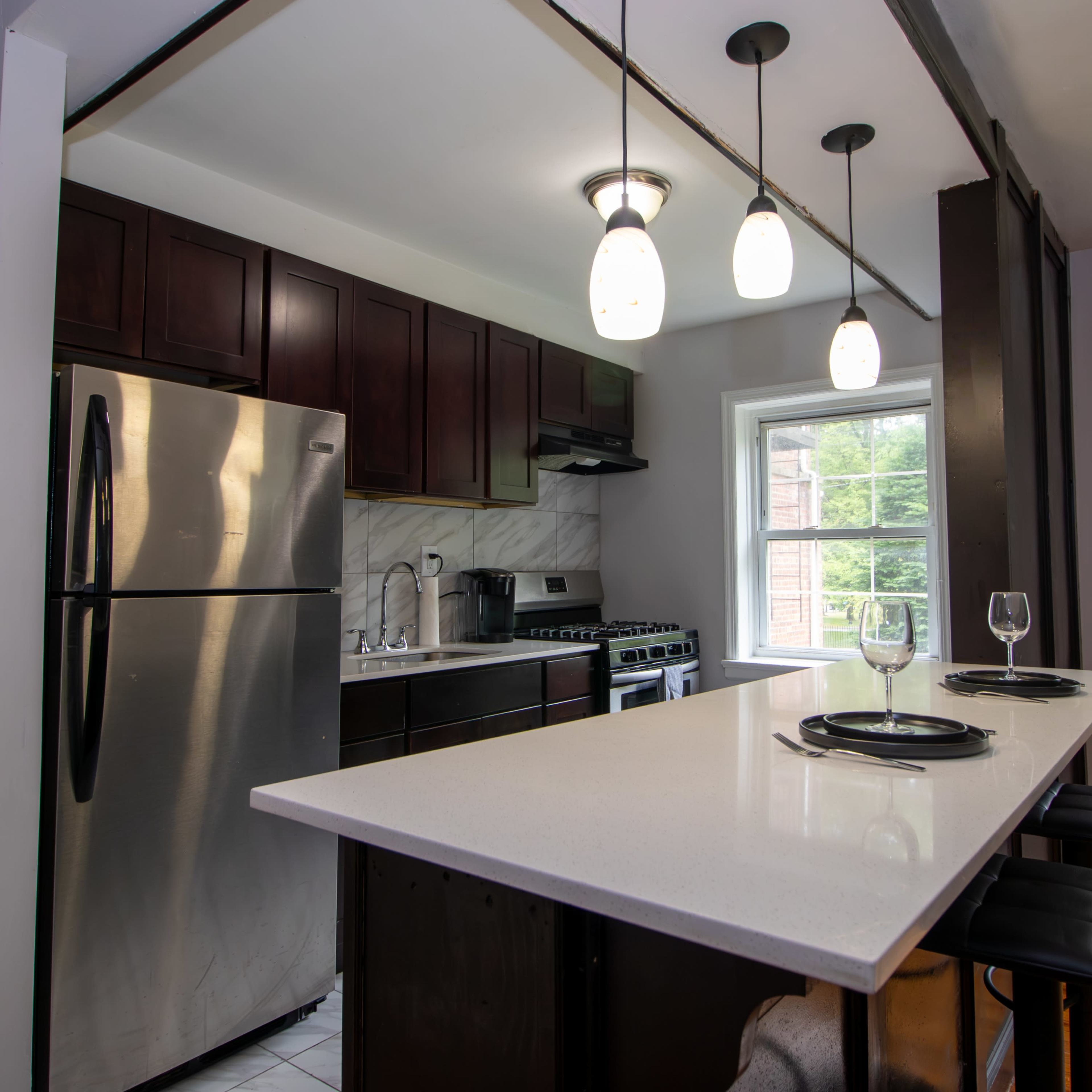 A modern kitchen features dark wood cabinets, stainless steel appliances, and a white countertop with bar seating.